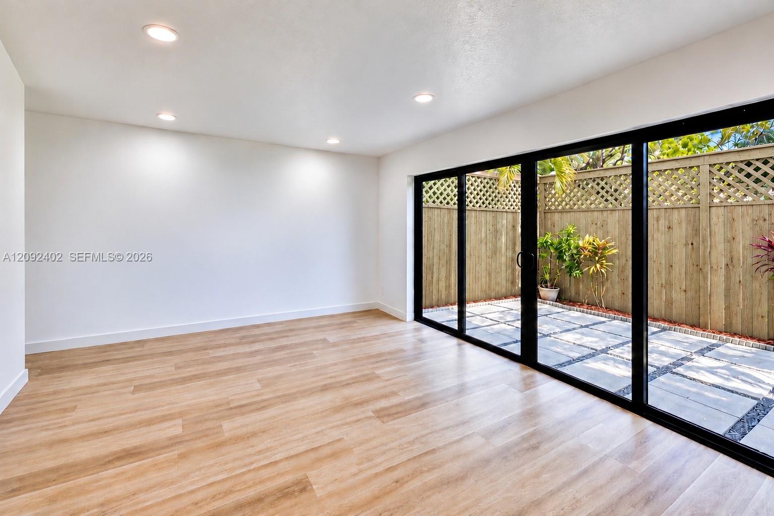 Interior space featuring wood-finish flooring, recessed lighting, and expansive black-framed sliding glass doors opening to a private patio with stone pavers and wooden lattice-topped fencing