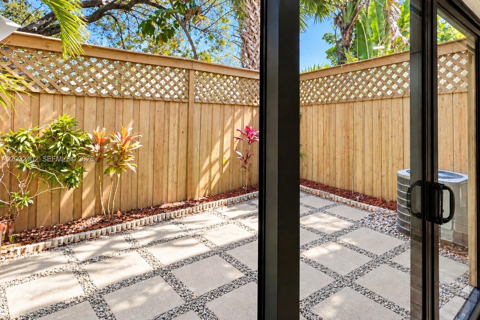 Private patio featuring concrete pavers with stone-filled grid detailing, enclosed by a wood privacy fence with lattice trim and landscaped border beds