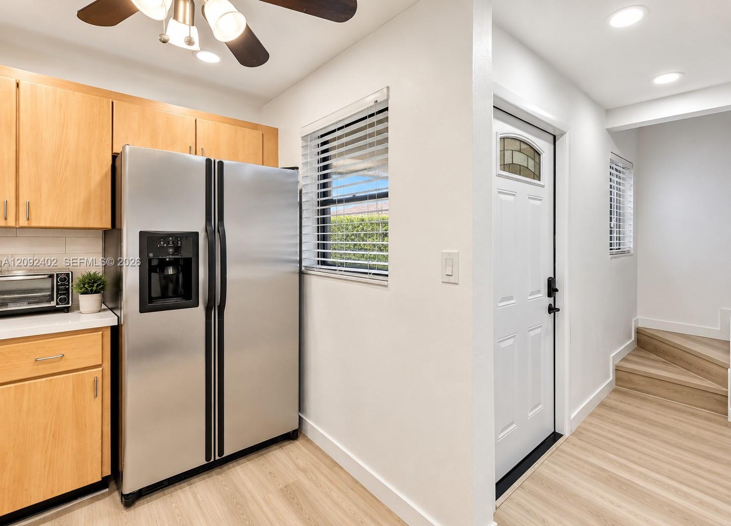 Kitchen featuring light-finish cabinetry, stainless steel side-by-side refrigerator, recessed lighting, wood-finish flooring, and a white exterior entry door with a decorative glass insert
