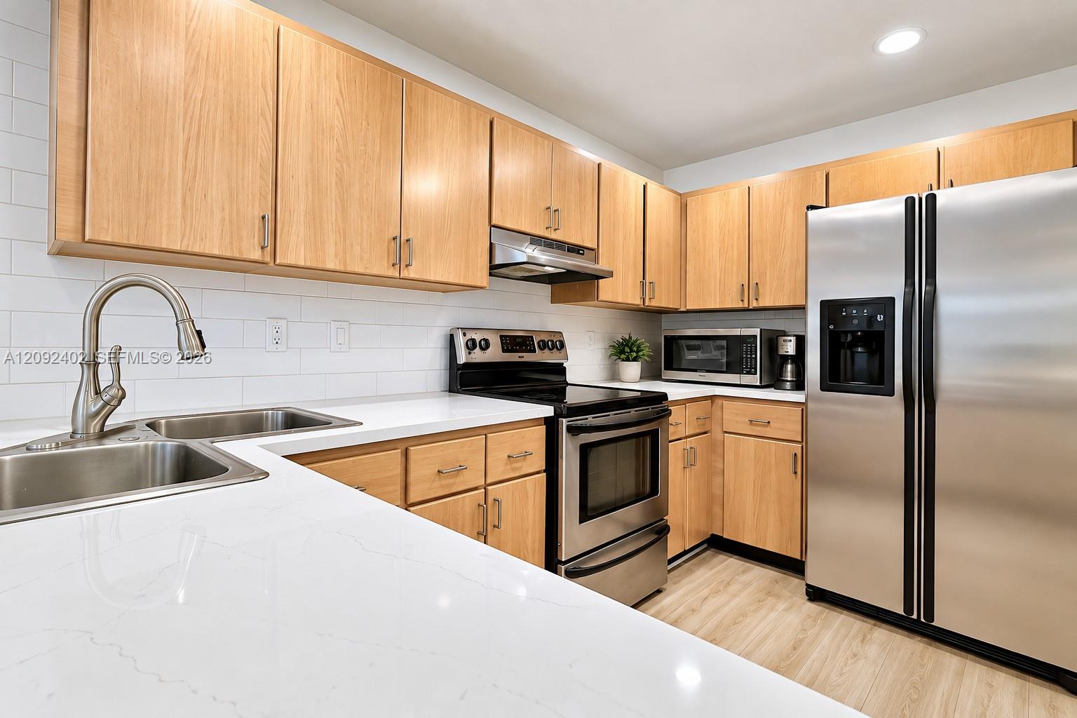 Kitchen featuring natural wood-finish cabinetry, white solid-surface countertops, subway tile backsplash, stainless steel appliances, and recessed lighting