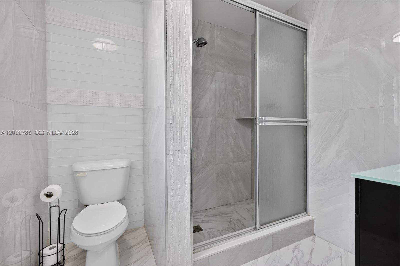 Bathroom featuring large-format gray tile shower surrounds, glass sliding shower enclosure, recessed shower shelving, and vertical white wall tile accents