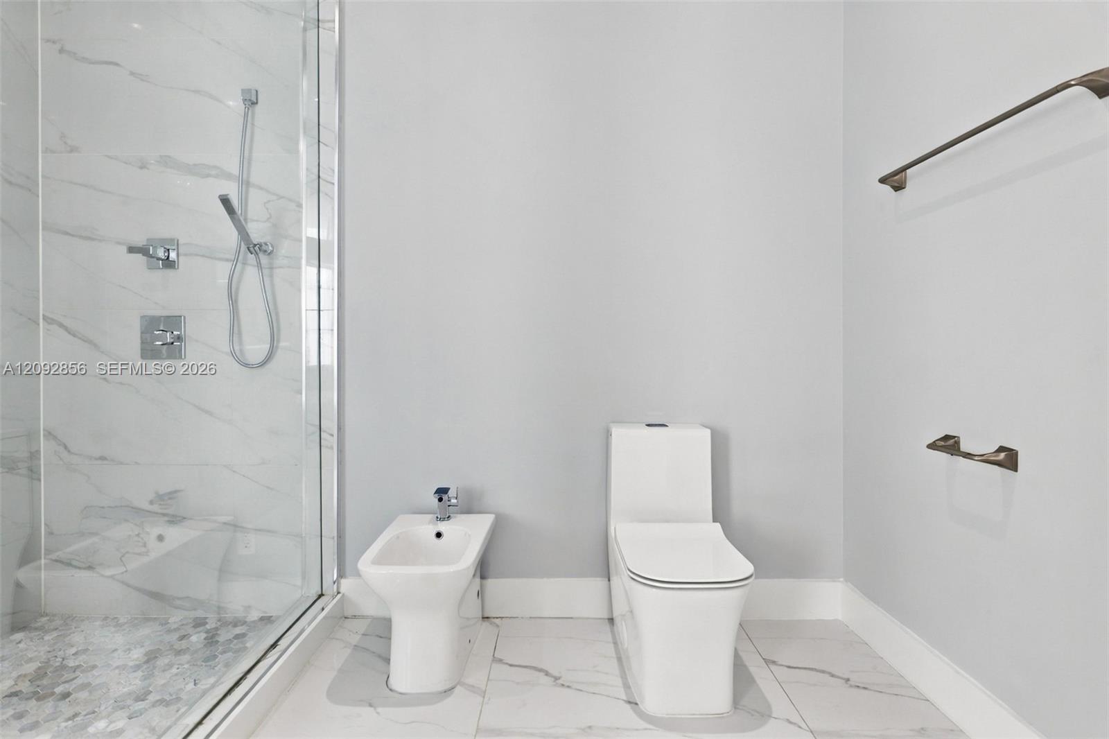 Walk-in shower with stone-look wall tile and pebble-texture flooring, integrated bidet, dual-flush toilet, and metal wall-mounted fixtures
