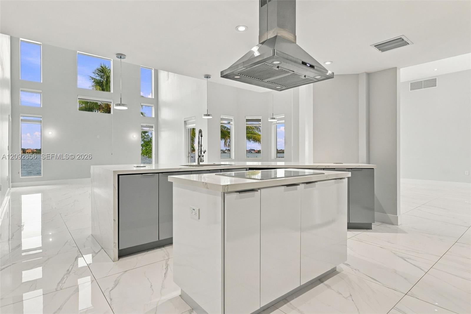 Kitchen featuring a central island with a solid surface countertop, stainless steel vent hood, floor-to-ceiling windows, high-gloss cabinetry, and large-format tile flooring