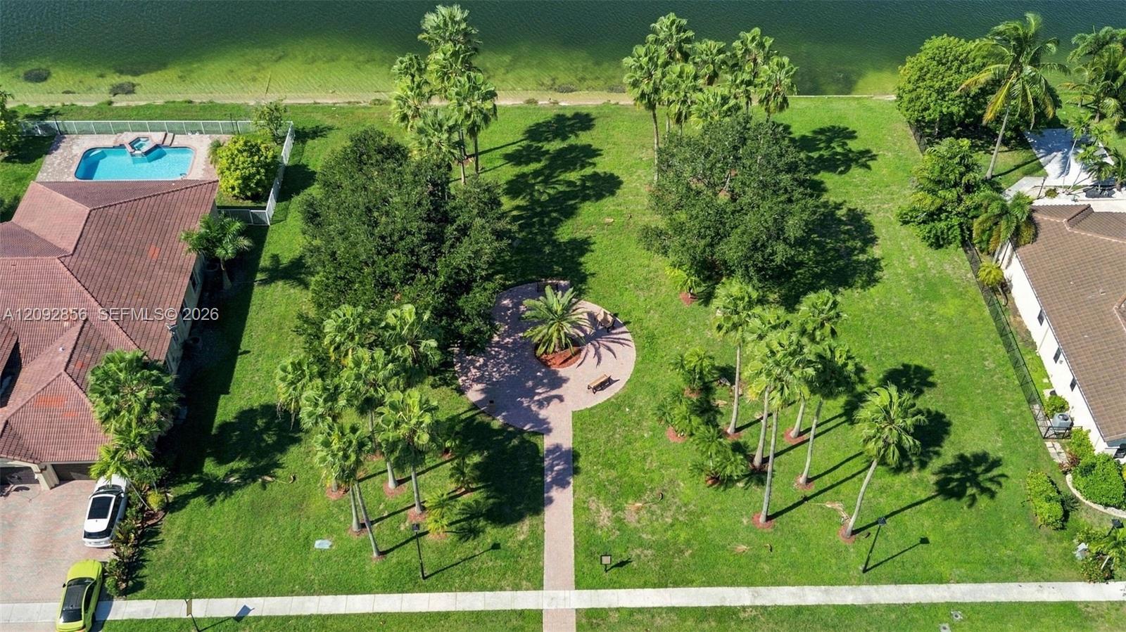 Expansive waterfront lot featuring mature landscaping, a paved stone pathway, a circular hardscape patio, and an in-ground swimming pool