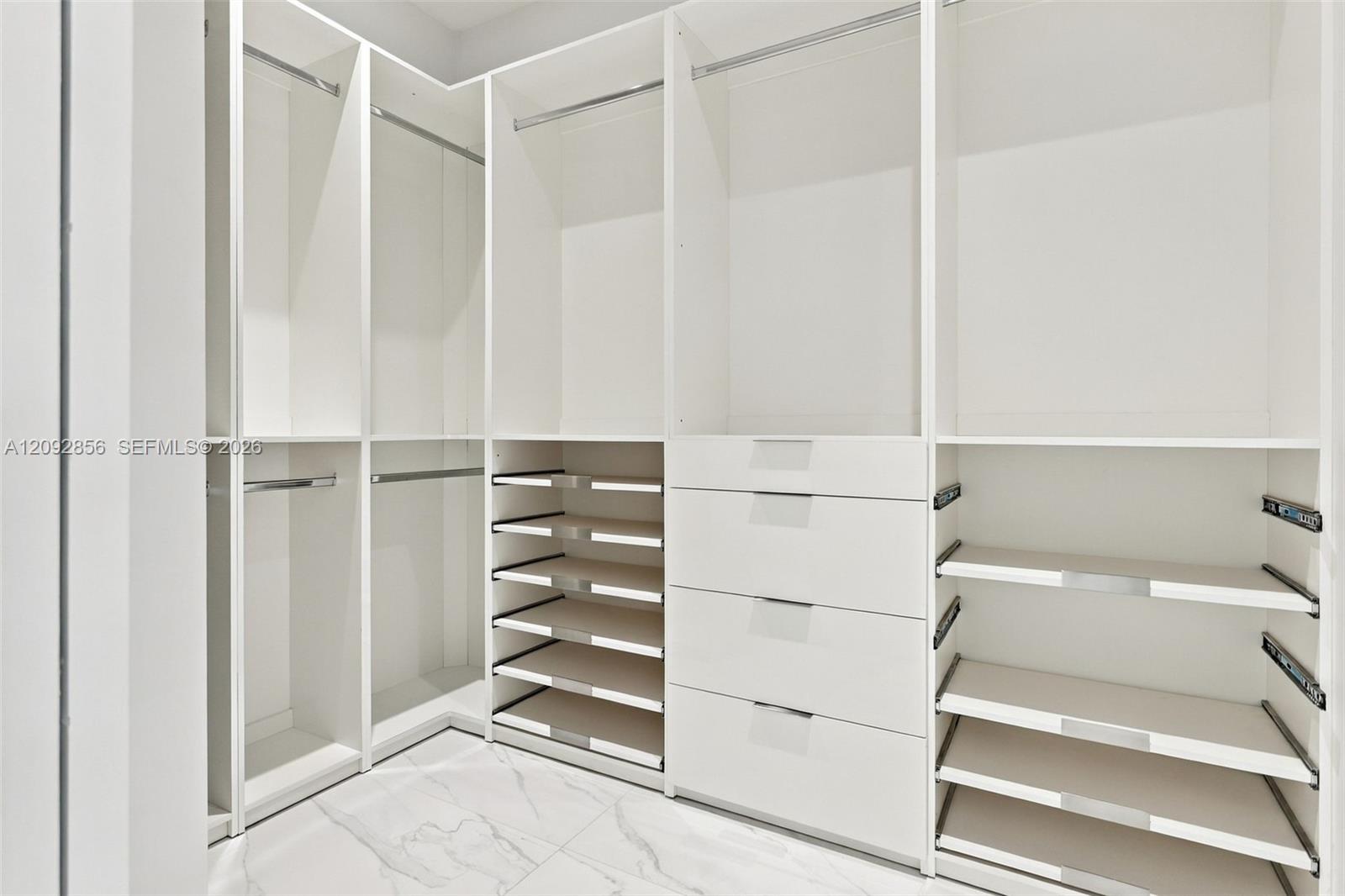 Custom built-in storage system featuring white cabinetry, multiple hanging sections, integrated shelving, and a four-drawer stack, complemented by large-format tile flooring