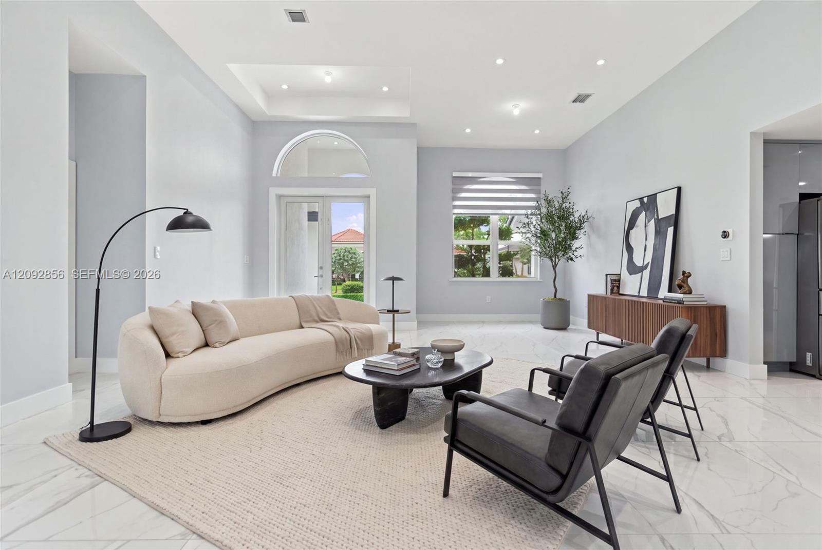 Virtually staged - Living area featuring a double-tray ceiling, recessed lighting, arched transom window, glass-paneled door, and large-format tile flooring