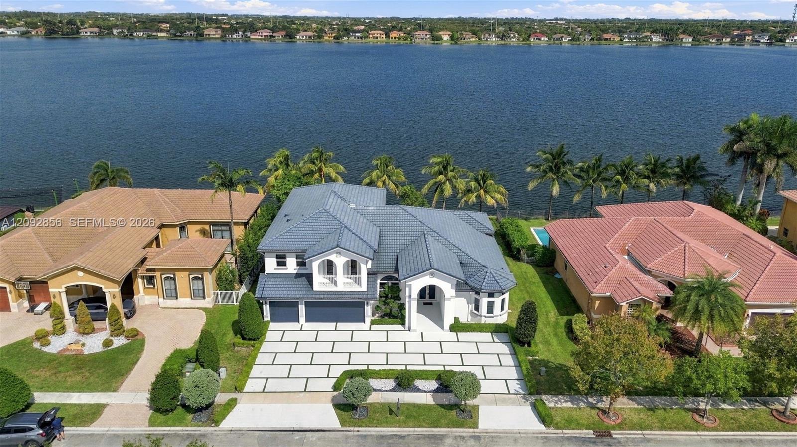 Waterfront property featuring a multi-gabled roofline, light-toned exterior finish, paver-style driveway, and an expansive rear lawn