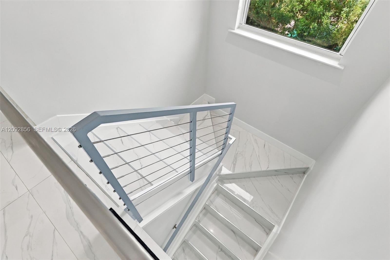 Staircase featuring white stone-finish tile flooring, metal cable railing, and a window