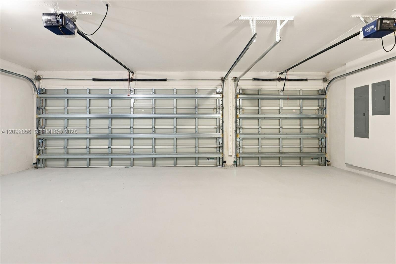 Two-car garage featuring dual overhead automatic openers, neutral flooring, and wall-mounted electrical panels