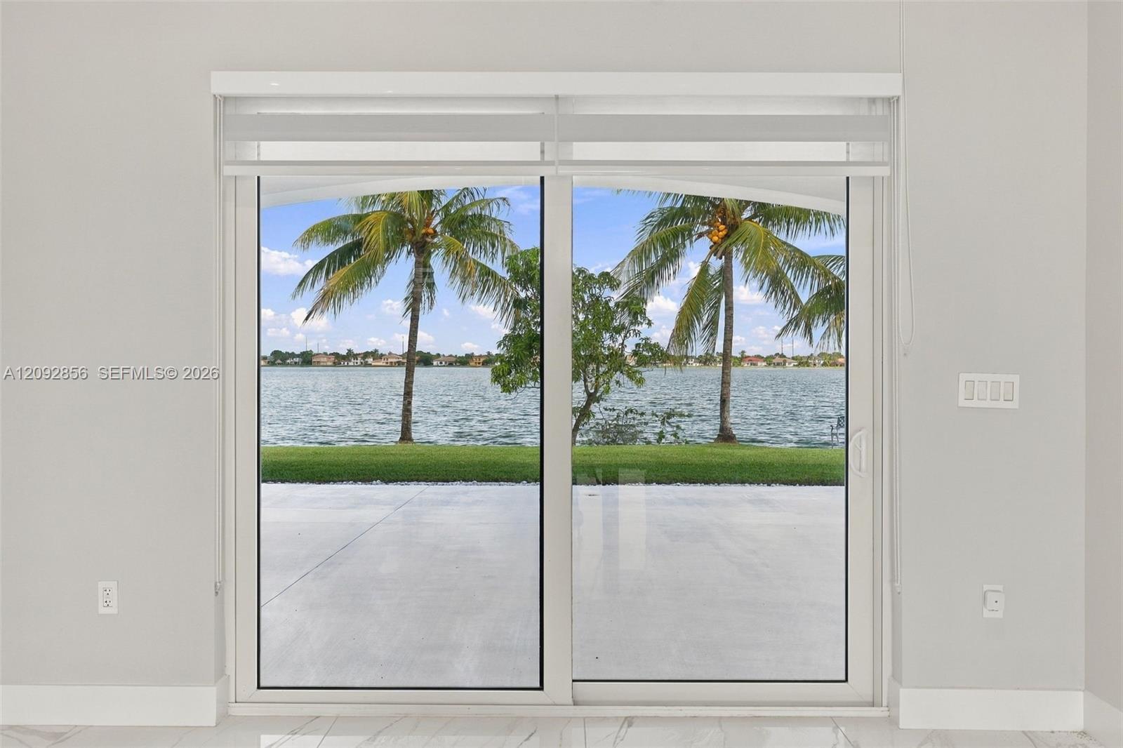 Large sliding glass door featuring white framing, polished stone flooring, and expansive water frontage with palm trees