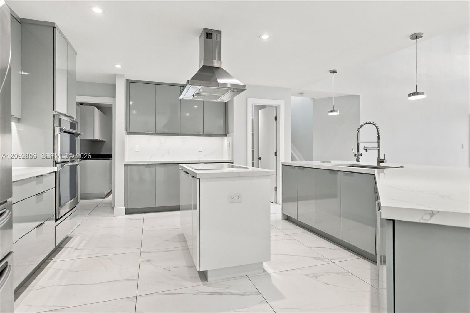Kitchen featuring high-gloss cabinetry, stone-finish countertops, stainless steel dual wall ovens, center island with cooktop, and large-format tiled flooring