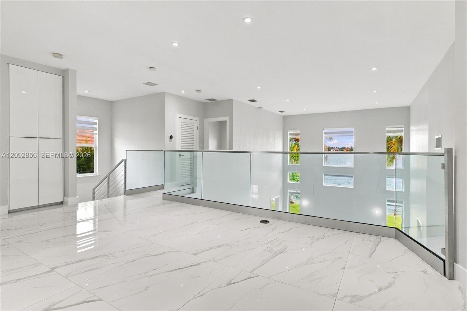 Open landing featuring high-gloss large-format tile flooring, glass panel railing with metallic hardware, recessed ceiling lighting, and floor-to-ceiling built-in cabinetry