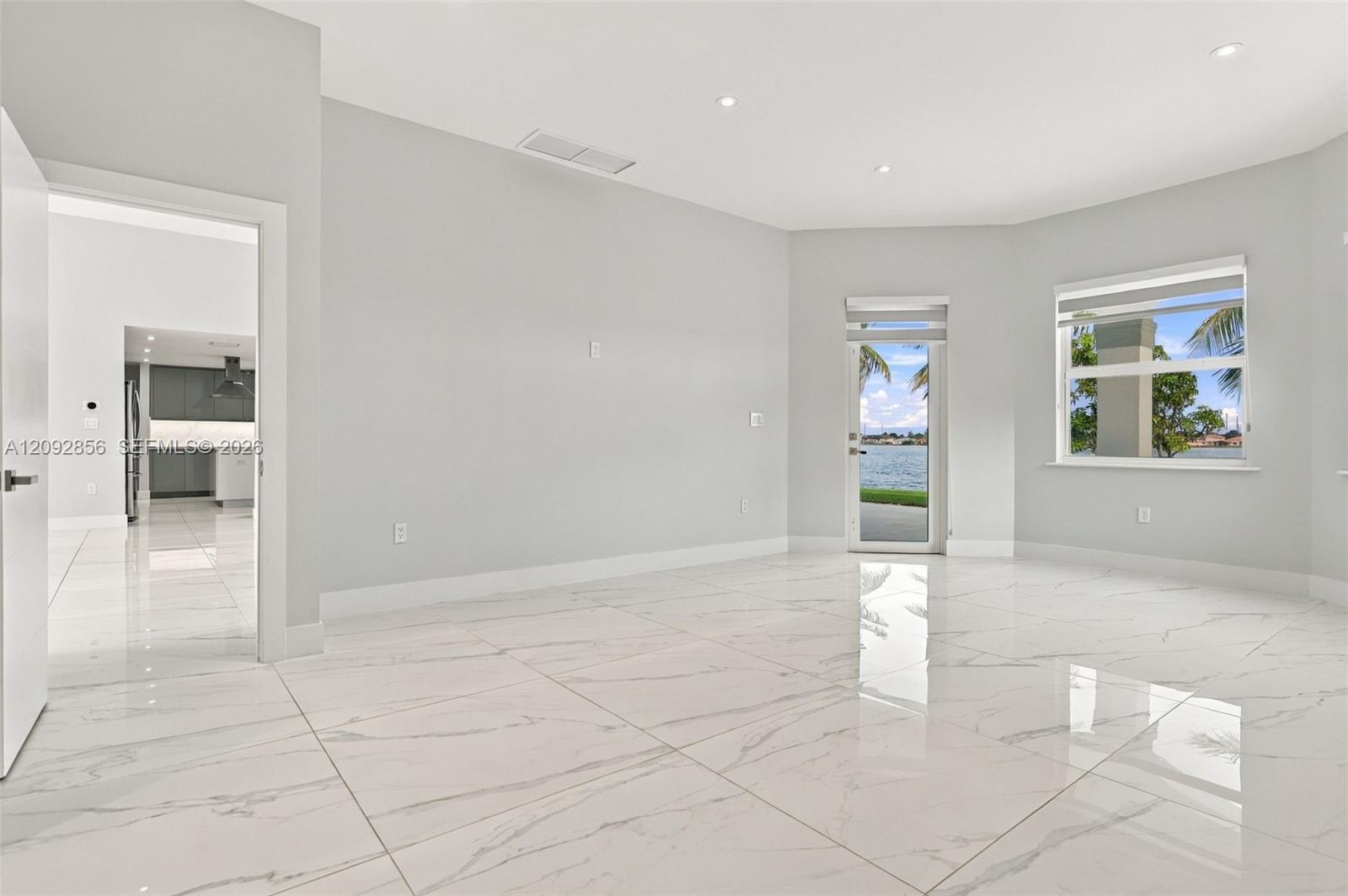 Polished stone-finish flooring, recessed lighting, neutral wall paint, and full-glass exterior door with waterfront scenery and access to back patio.