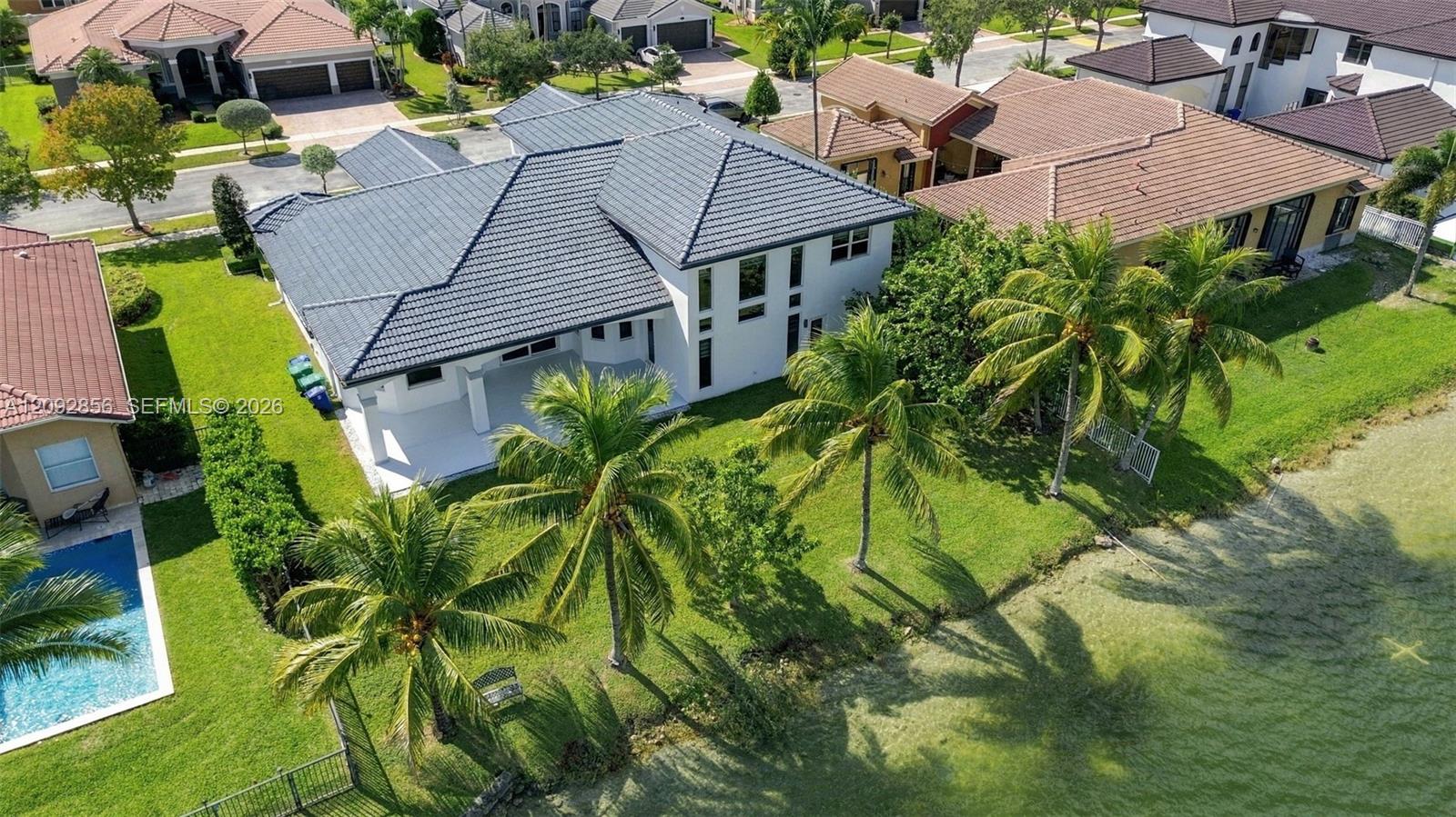 Multi-level residence featuring a tile roof, expansive rear patio, manicured lawn, and waterfront lot with mature palm trees