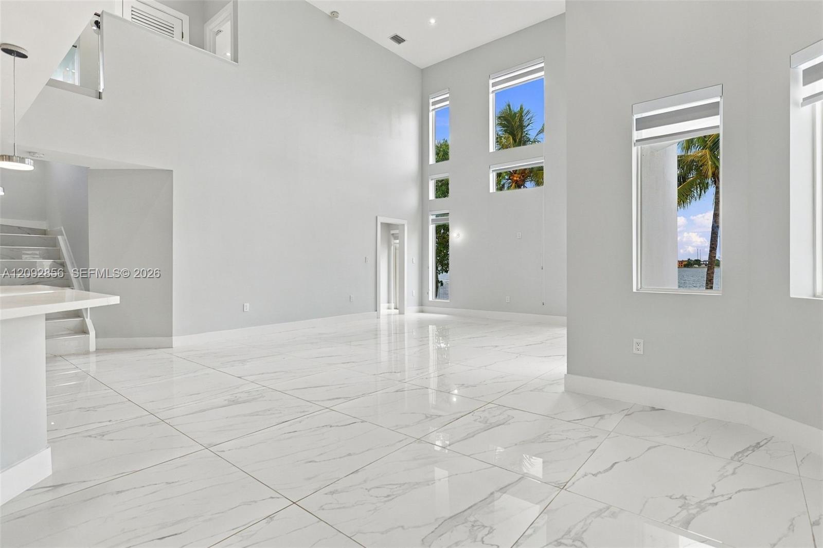 Double-height ceilings, large-format polished stone-finish floor tiles, multi-level oversized windows, and a built-in staircase with a glass railing