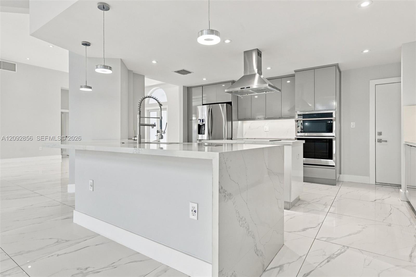 Kitchen featuring a stone-surface waterfall island, high-gloss cabinetry, stainless steel wall-mounted oven and microwave, stainless steel range hood, and large-format tile flooring