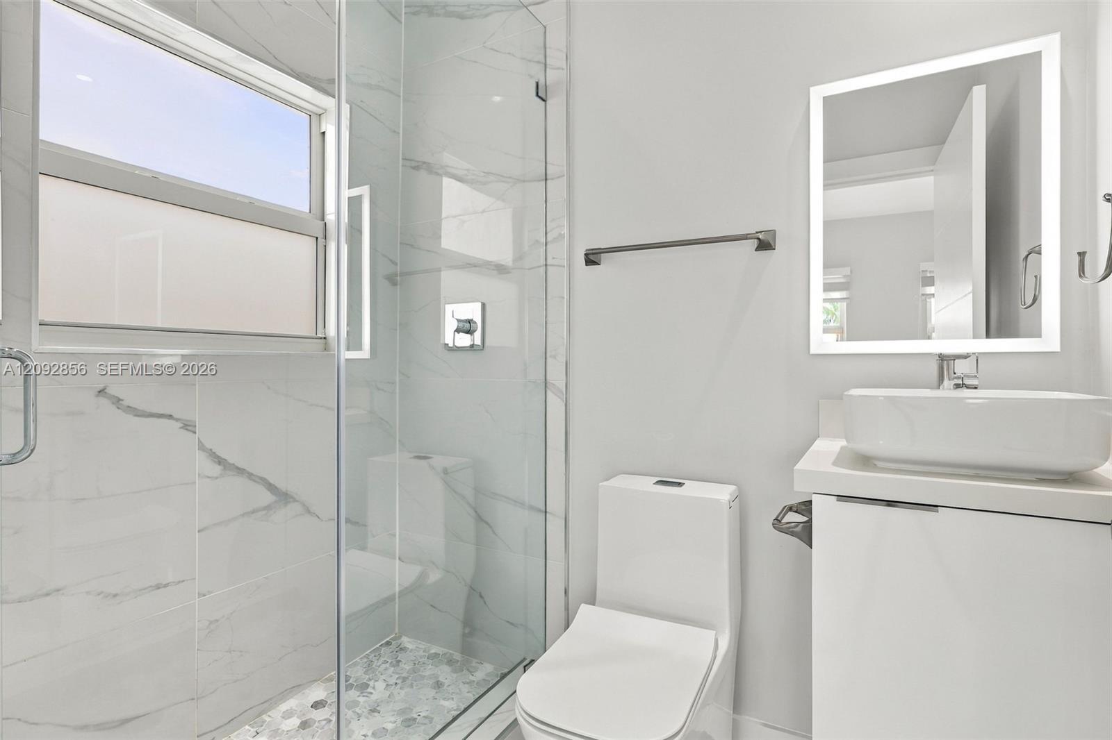 4th bathroom (Insuite) Bathroom featuring a glass-enclosed shower with floor-to-ceiling stone-pattern tile, a floating vanity with a rectangular vessel sink, and an LED-backlit mirror