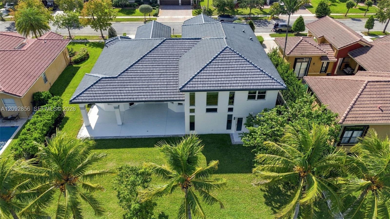 Two-story residence featuring a tile roof, light-toned exterior finish, covered patio, and landscaped yard with mature palms