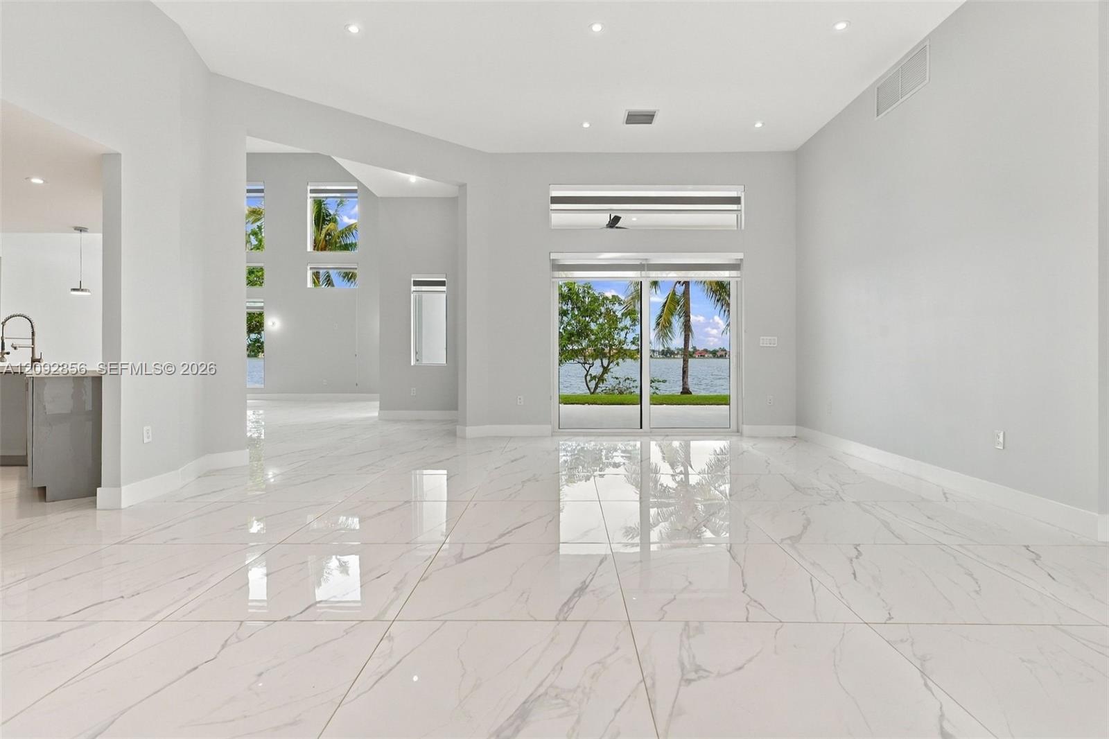 Open-concept interior featuring large-format polished tile flooring, recessed lighting, multi-level window configurations, and sliding glass doors with water frontage