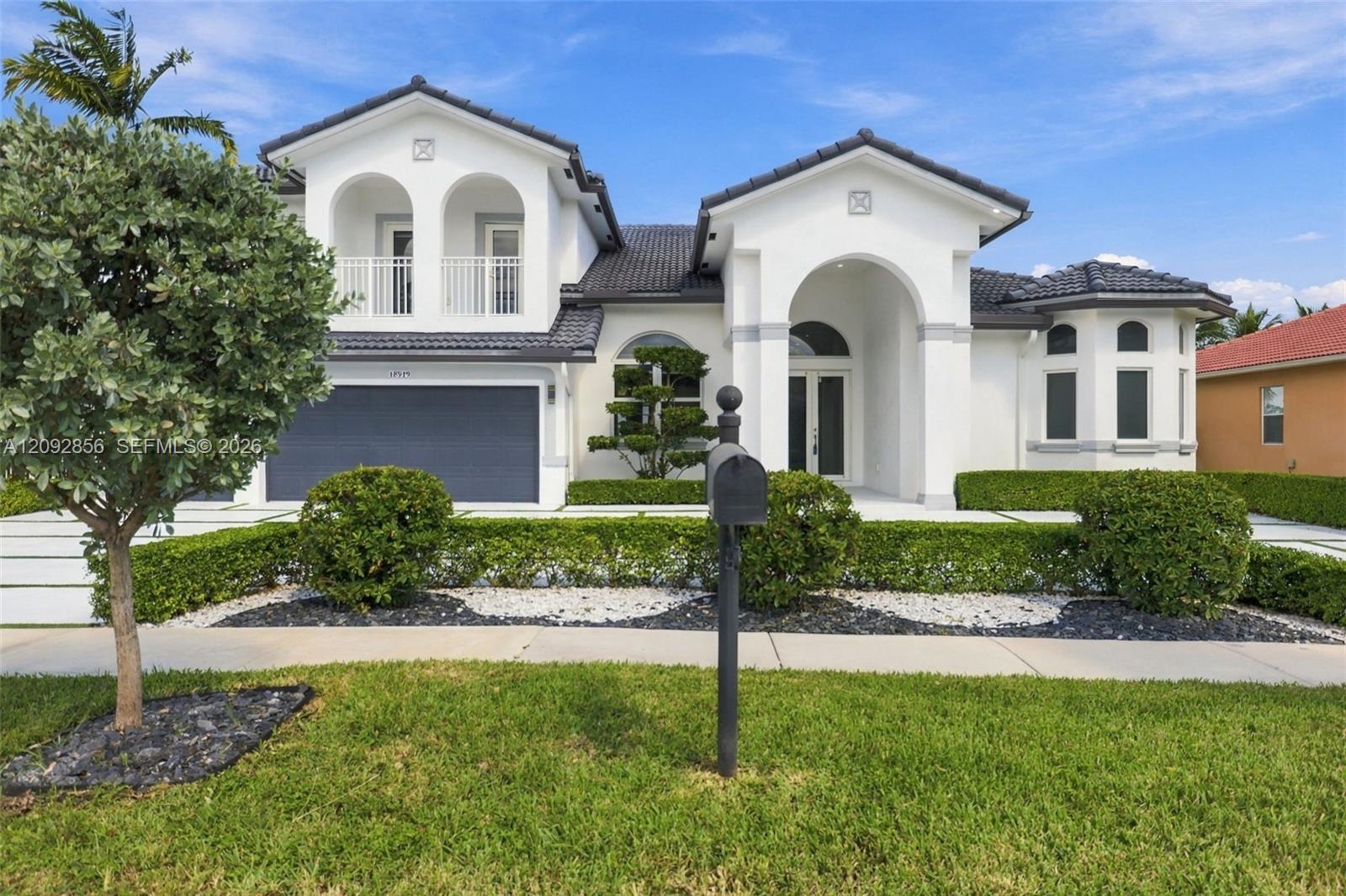 Two-story residence featuring a tile roof, arched entryway, upper-level balcony, and a multi-car garage with a concrete paver driveway
