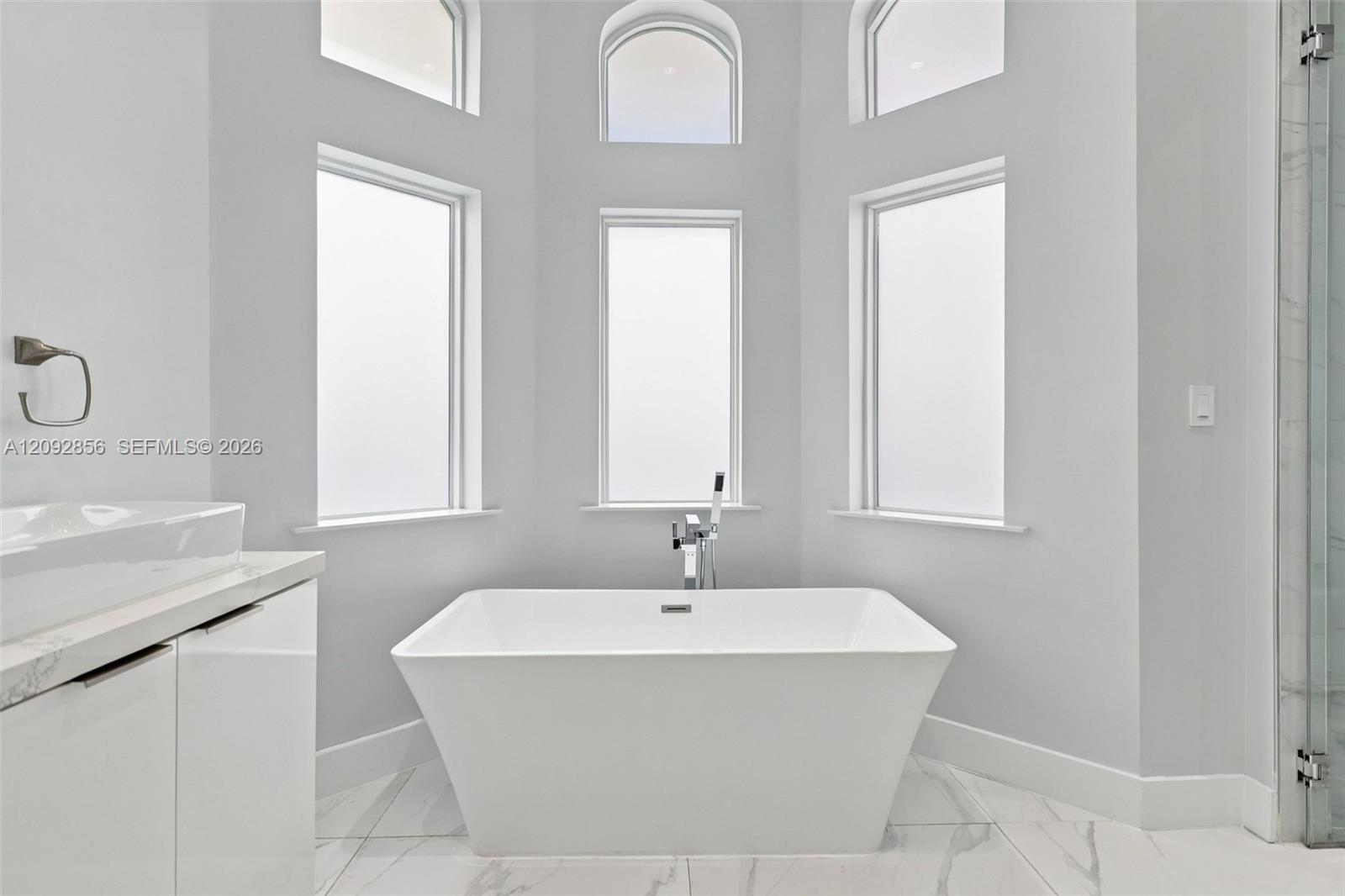 Freestanding rectangular soaking tub with a deck-mounted faucet, set against a wall of three tall windows topped by three arched transom windows