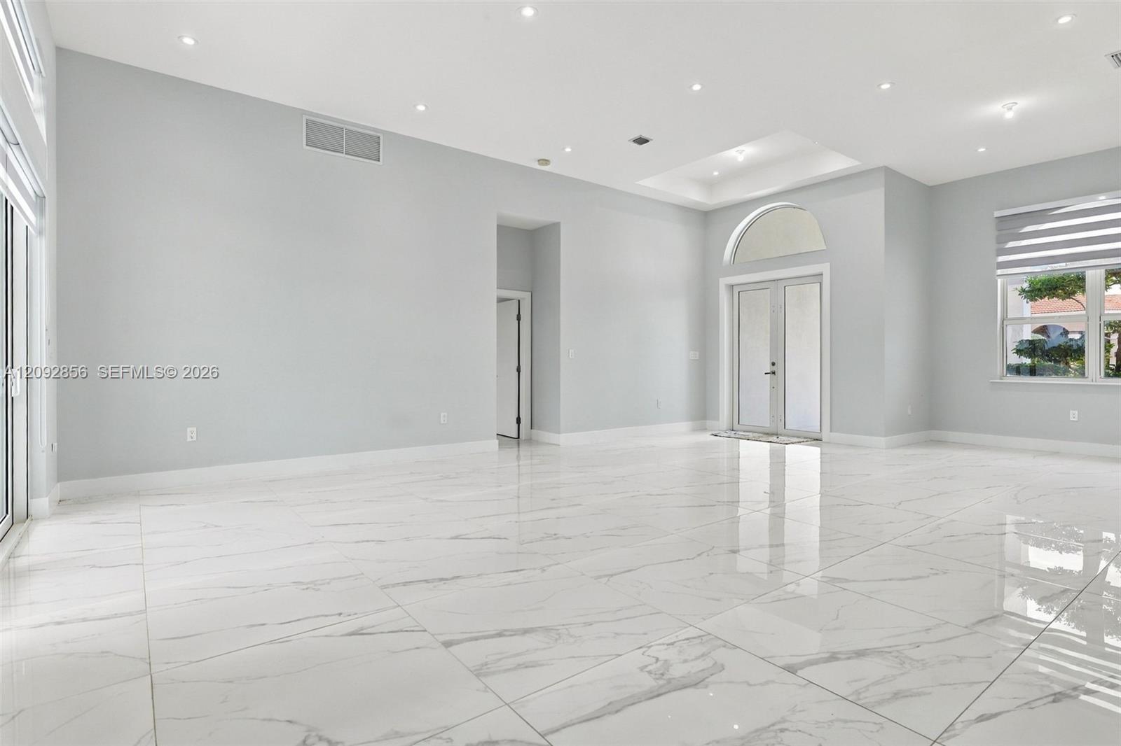 High-ceiling interior featuring polished tile flooring, recessed lighting, double glass doors with an arched transom, and a tray ceiling
