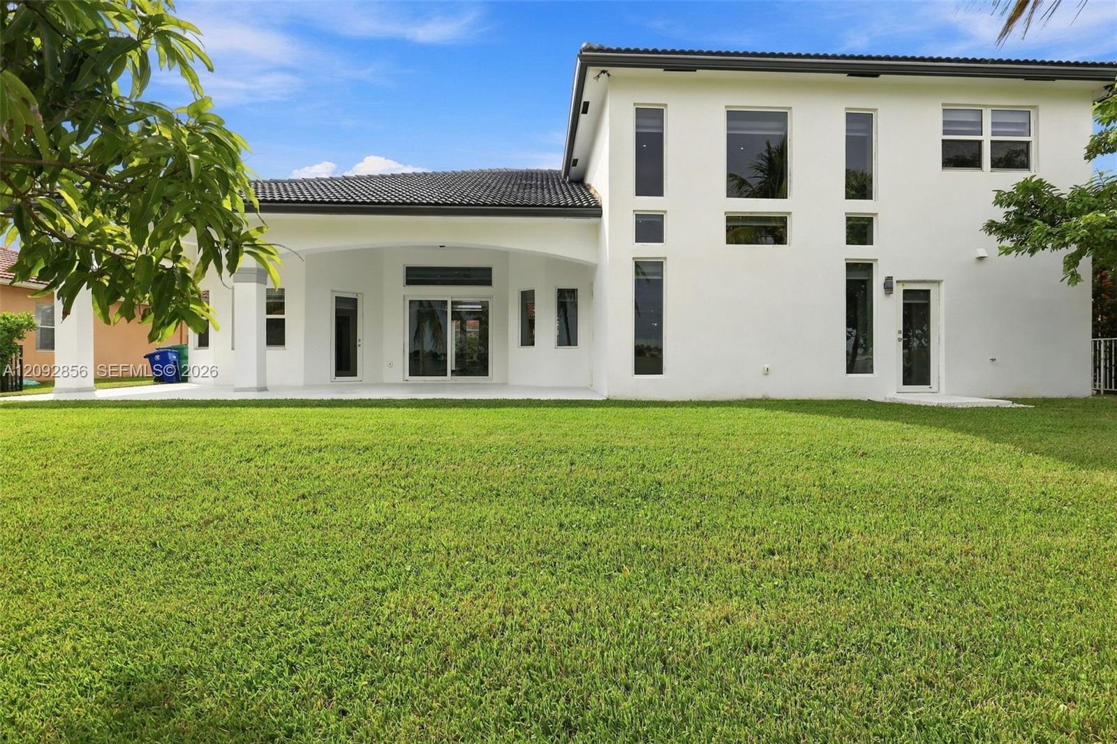 Two-story exterior featuring a stucco facade, tiled roof, covered patio, and multi-paned vertical windows