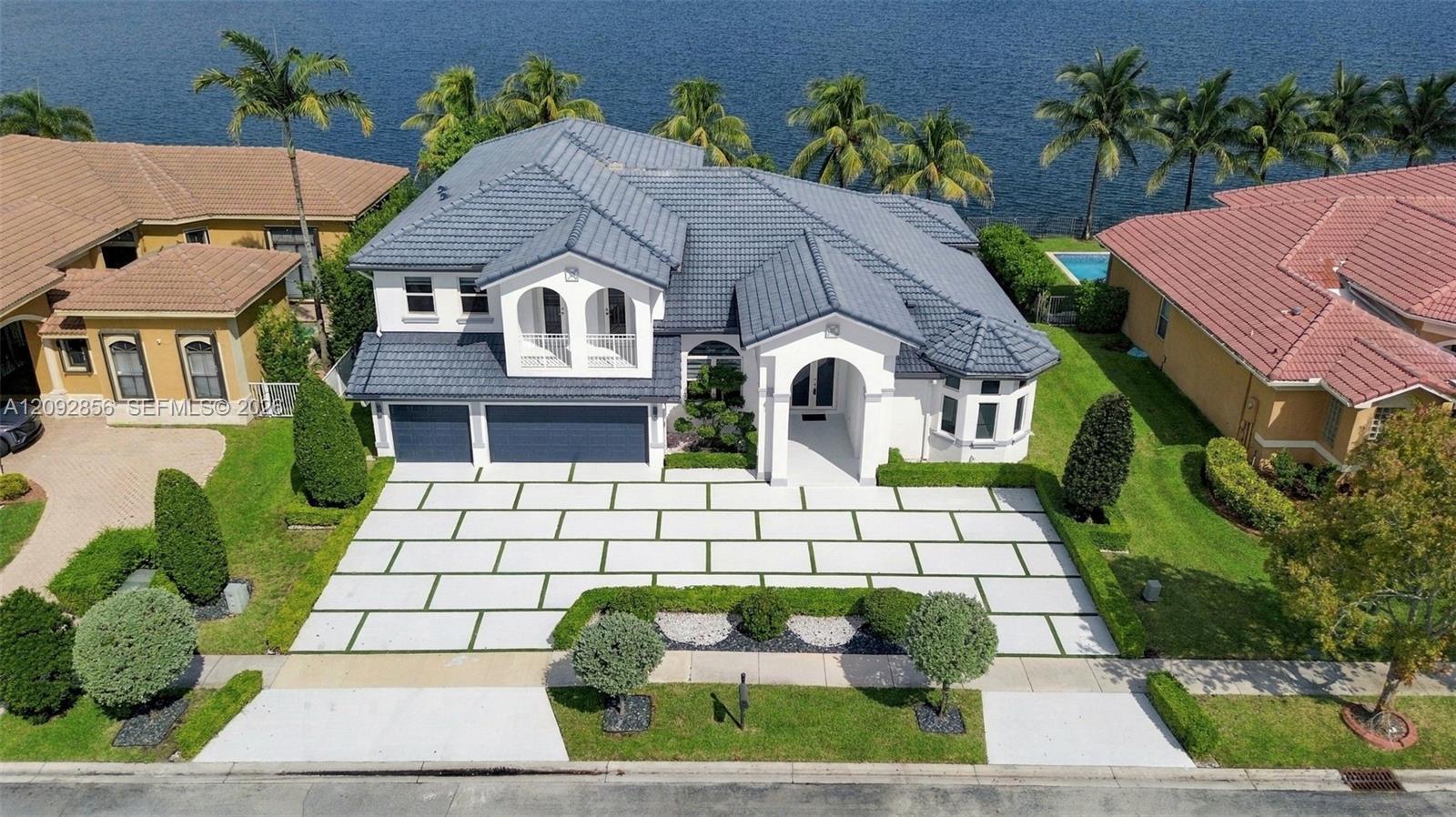 Waterfront estate featuring a concrete tile roof, paver driveway with grass inlay, arched architectural detailing, and a three-car garage