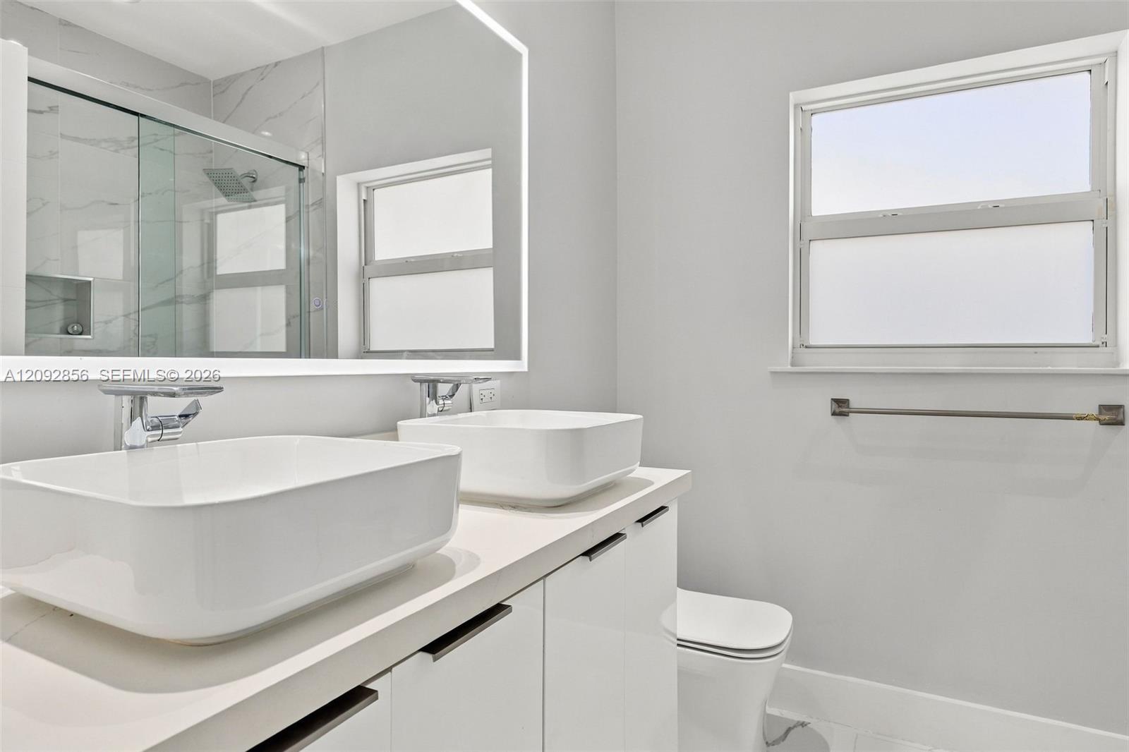 3rd bathroom - loft - Dual vessel sinks with chrome faucets, quartz-surfaced vanity, large backlit mirror, and glass-enclosed shower with tiled walls