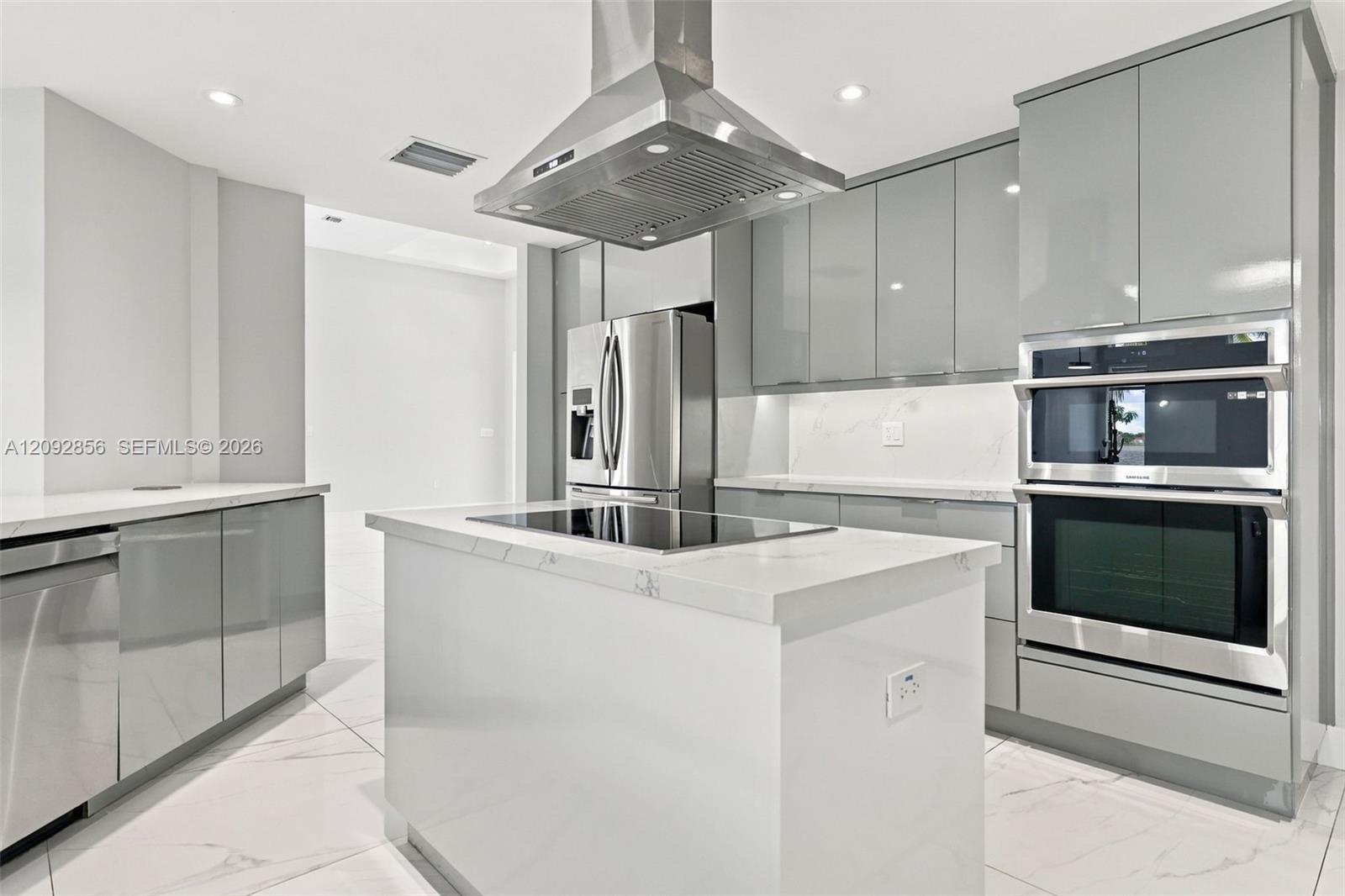 Kitchen featuring high-gloss gray cabinetry, stone-finish countertops, stainless steel appliances, a center island with an integrated cooktop, and an overhead stainless steel range hood