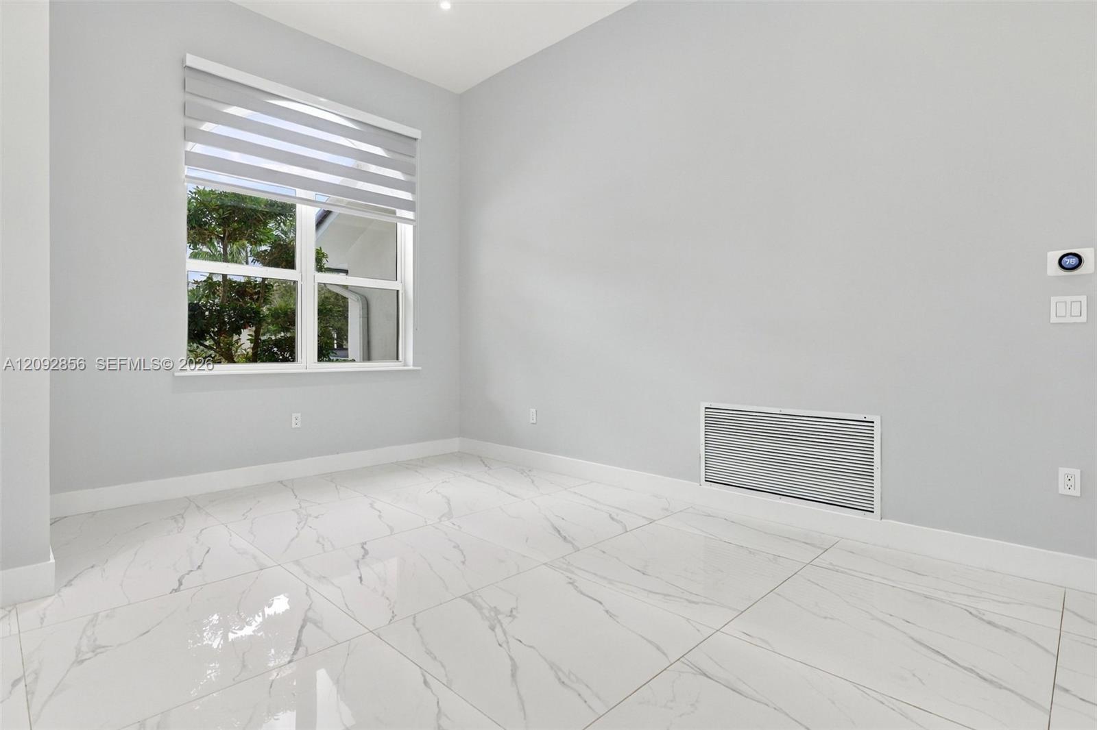 Large-format stone-finish floor tiles, neutral wall paint, and a window with a multi-layered roller shade