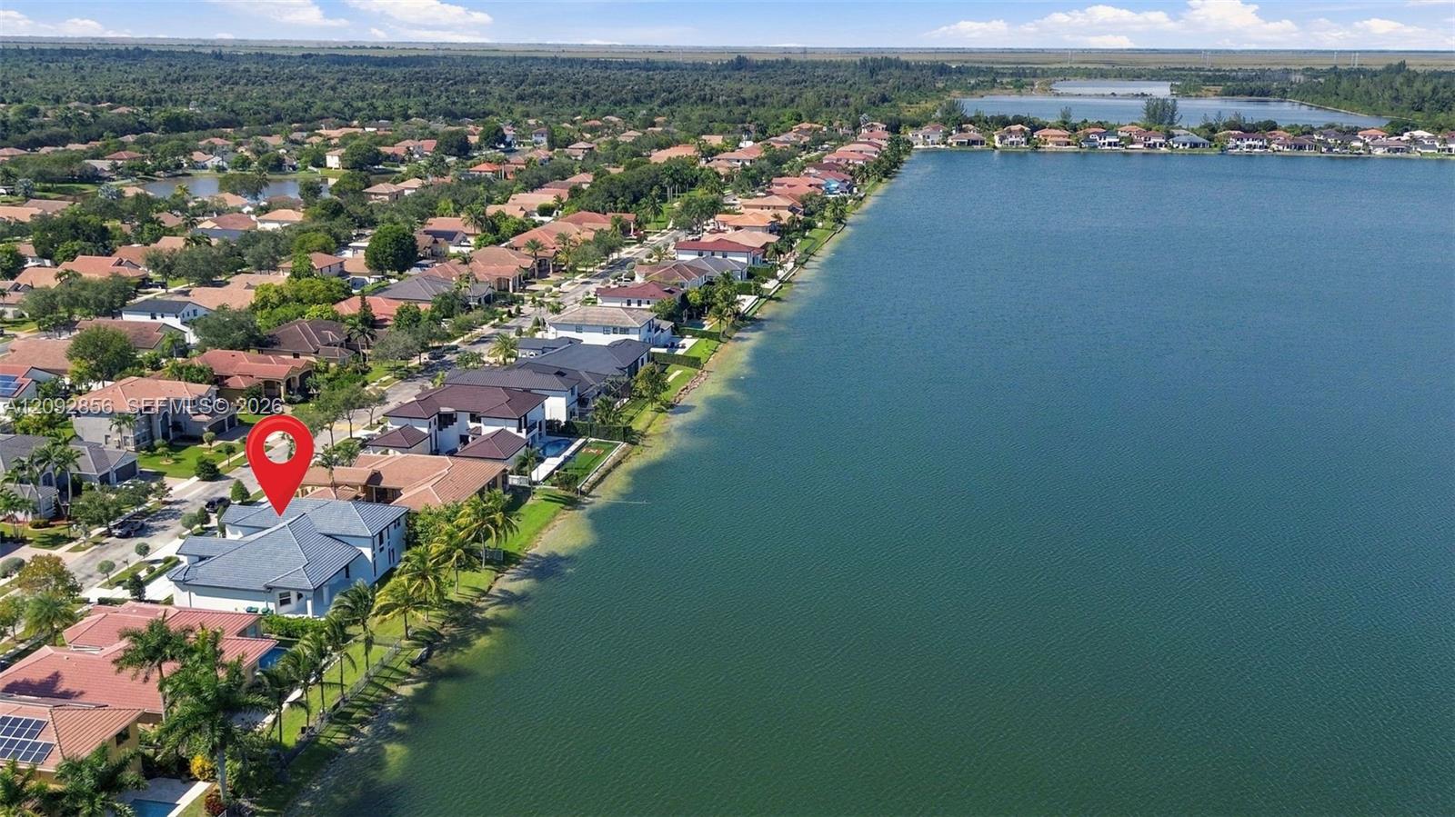 Aerial perspective of waterfront property featuring direct lake access, tile roofing, and mature perimeter landscaping