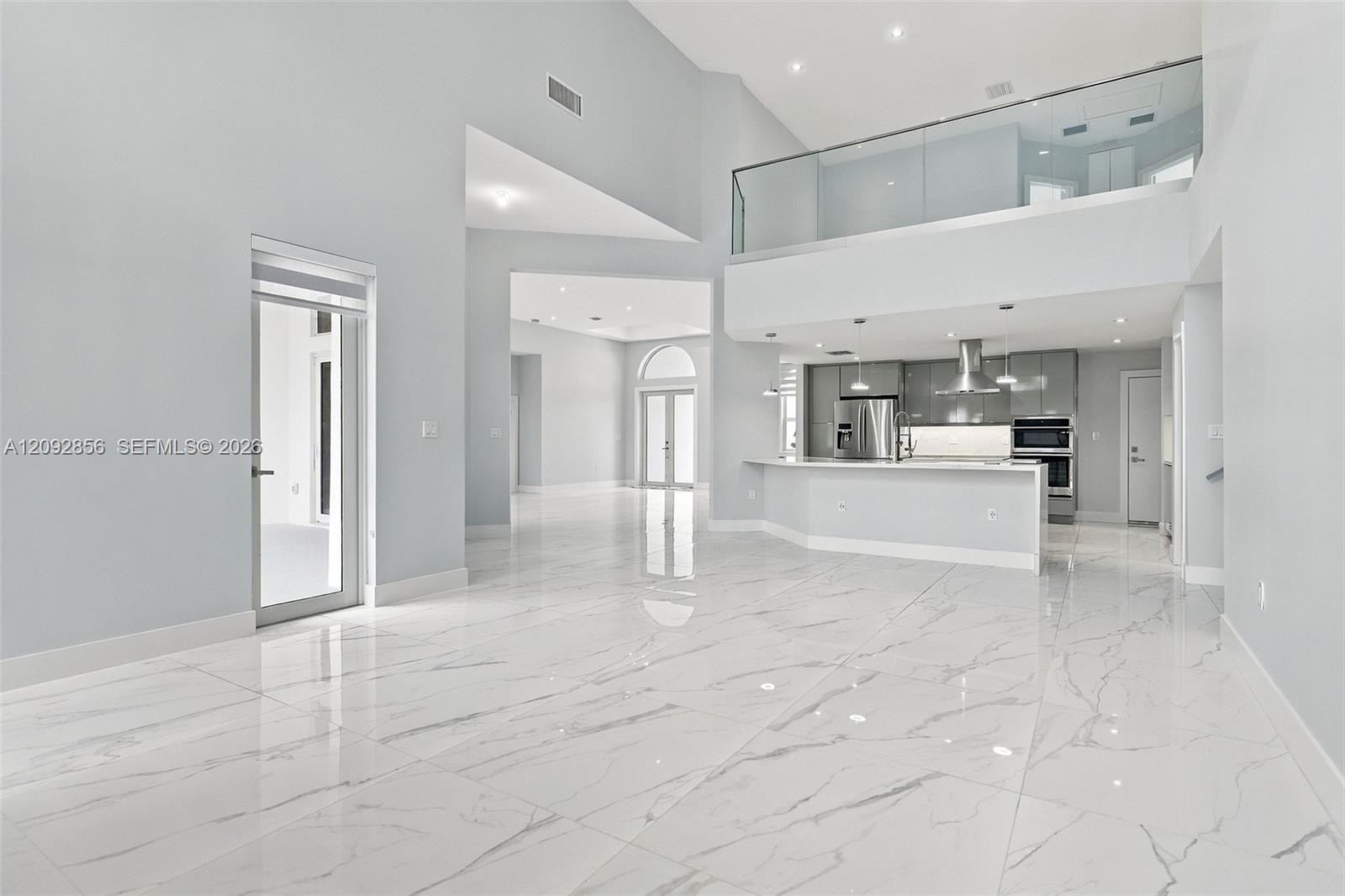Open-concept interior with vaulted ceilings, large-format veined tile flooring, glass-panel balcony railing, stainless steel built-in appliances, and recessed lighting