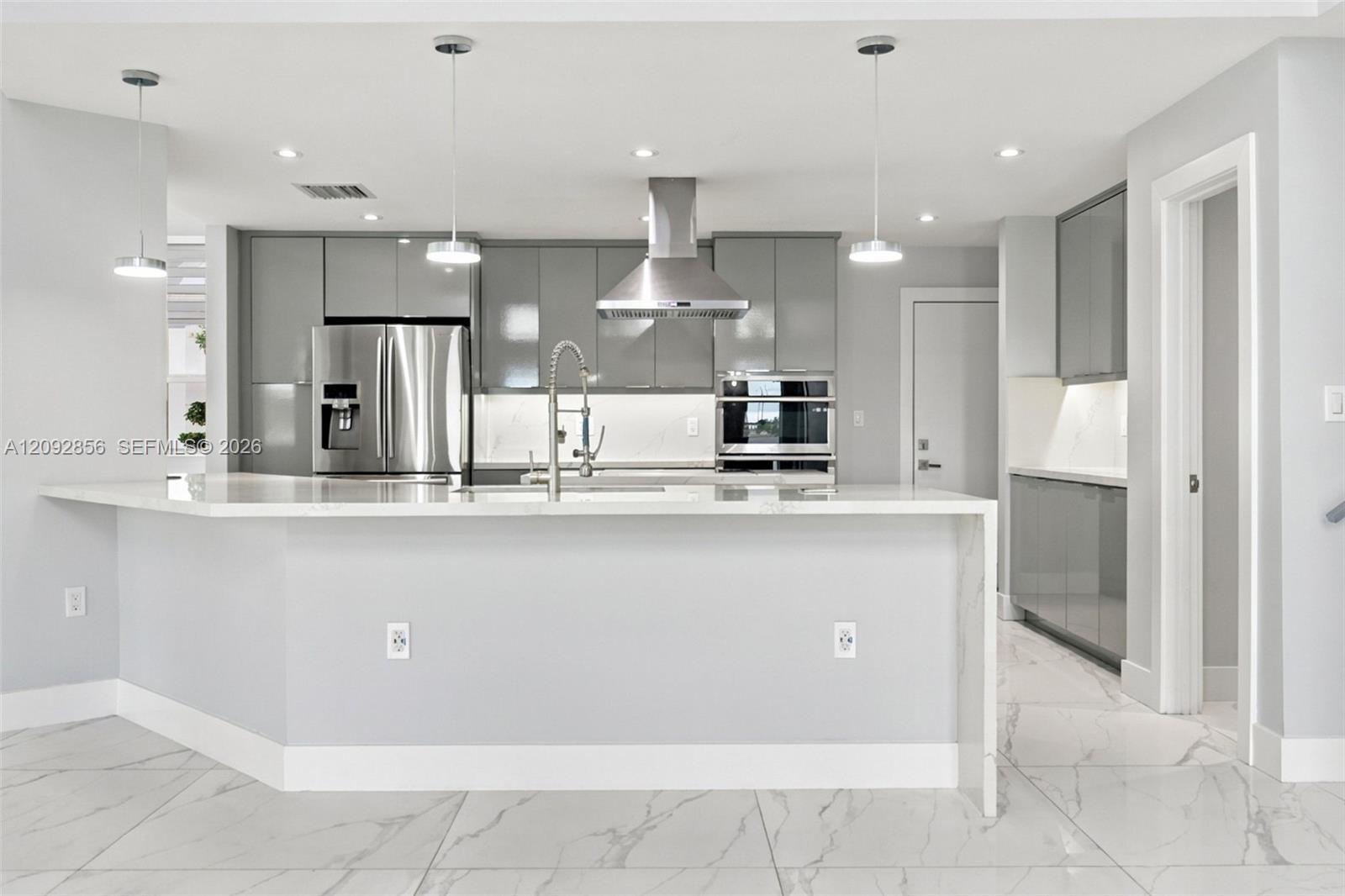 Kitchen featuring high-gloss cabinetry, stone-surface waterfall island, stainless steel appliances, built-in range hood, and large-format tile flooring