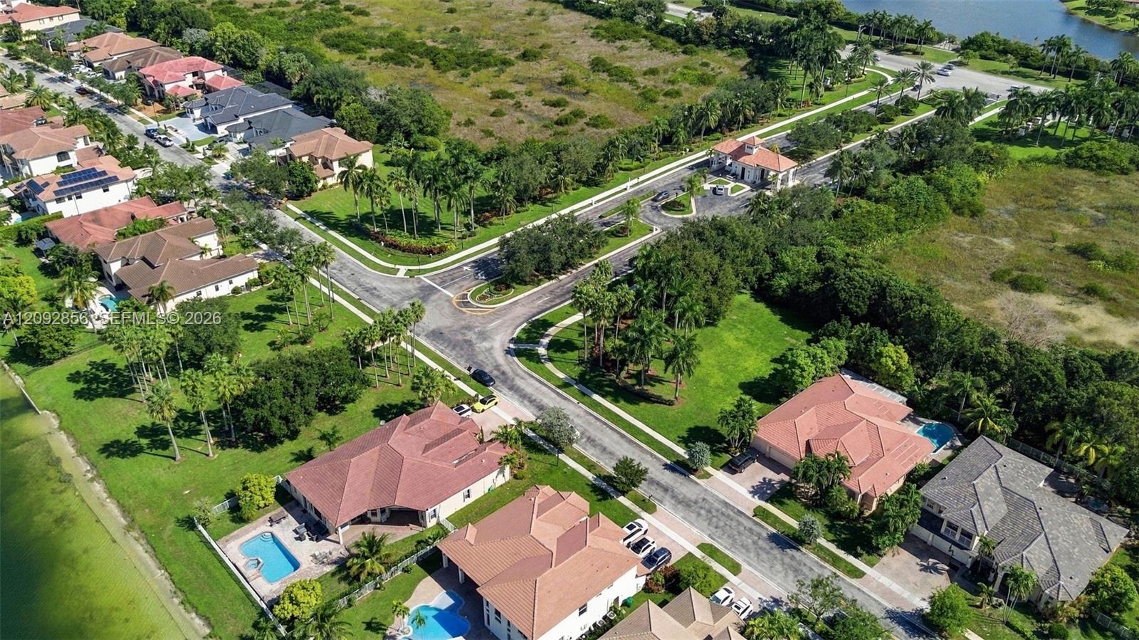Aerial perspective of a residential community featuring multi-hipped tile roofing, paved streets, private swimming pools, and mature landscaping throughout the grounds