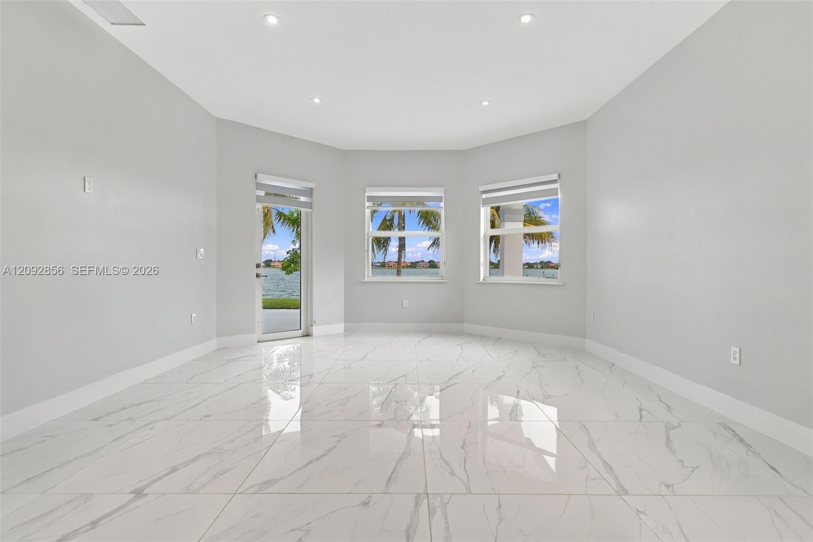Spacious room featuring polished tile flooring with a marble-pattern finish, recessed ceiling lighting, a multi-paneled bay window configuration, and a glass-paneled exterior door