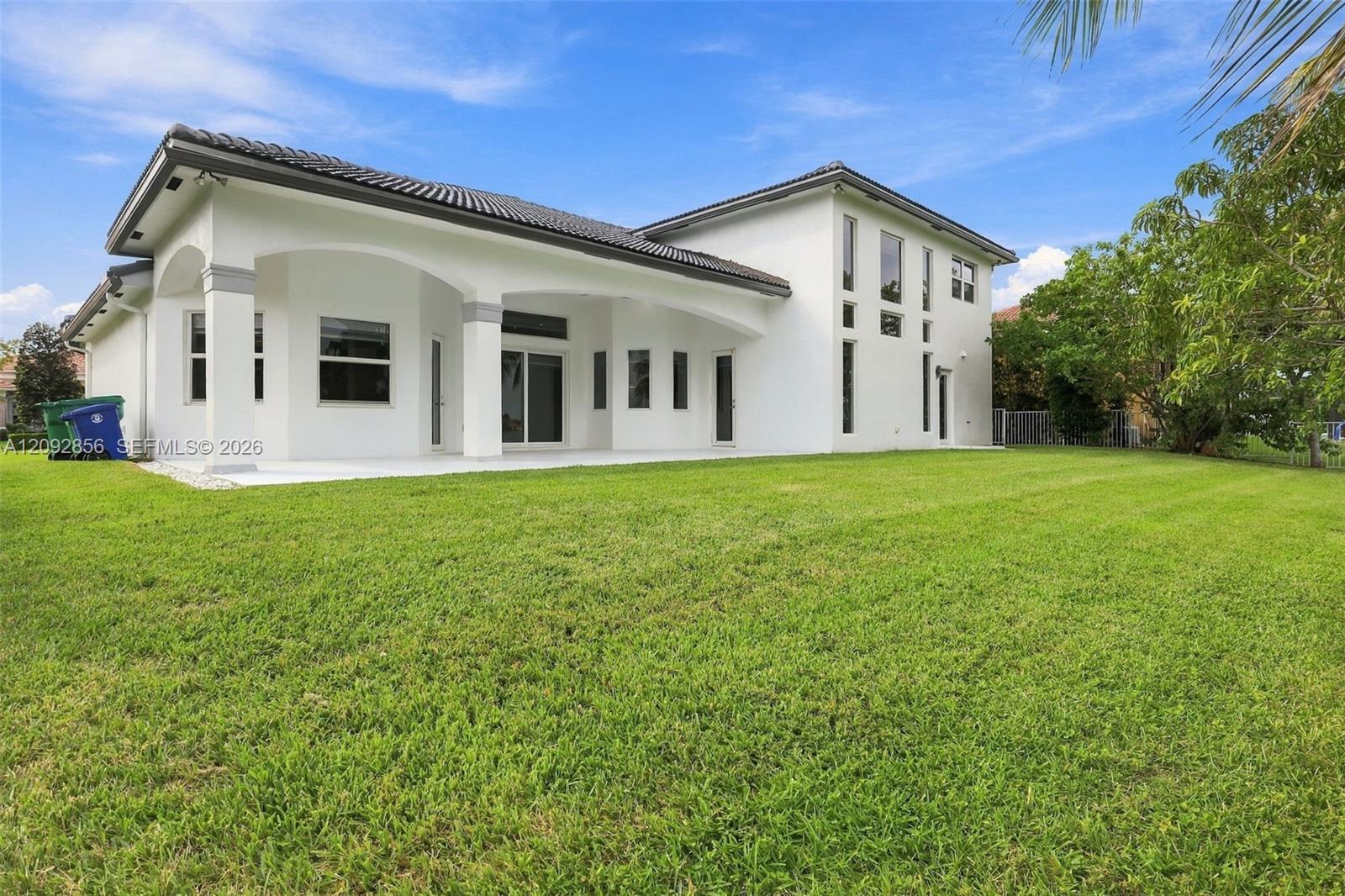 Exterior featuring a multi-story stucco facade, a tile roof, an arched covered patio, and an expansive lawn