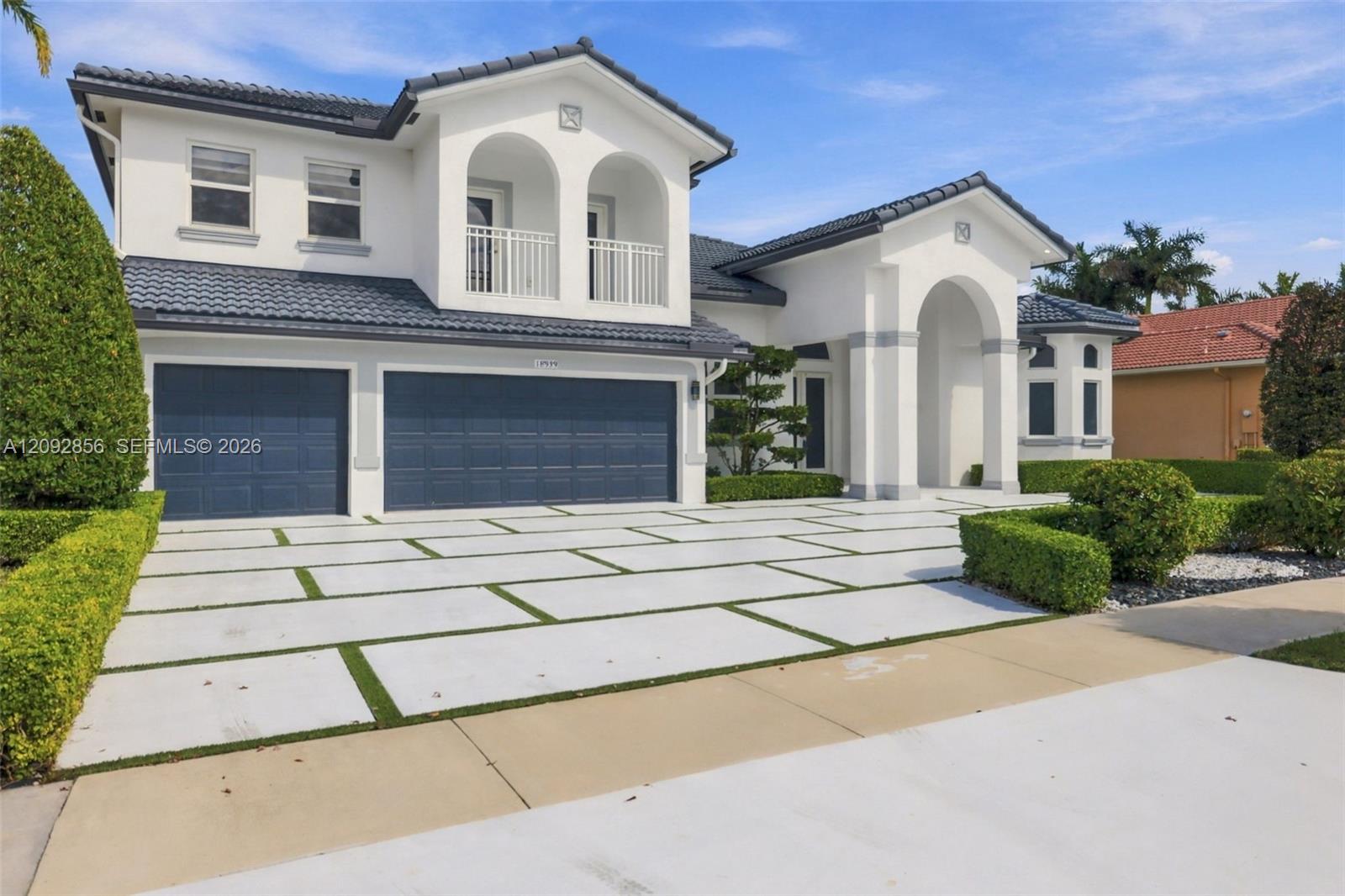 Mediterranean-style exterior featuring a tile roof, stucco finish, three-car garage, covered entryway with arched columns, and a paved driveway with integrated lawn grid