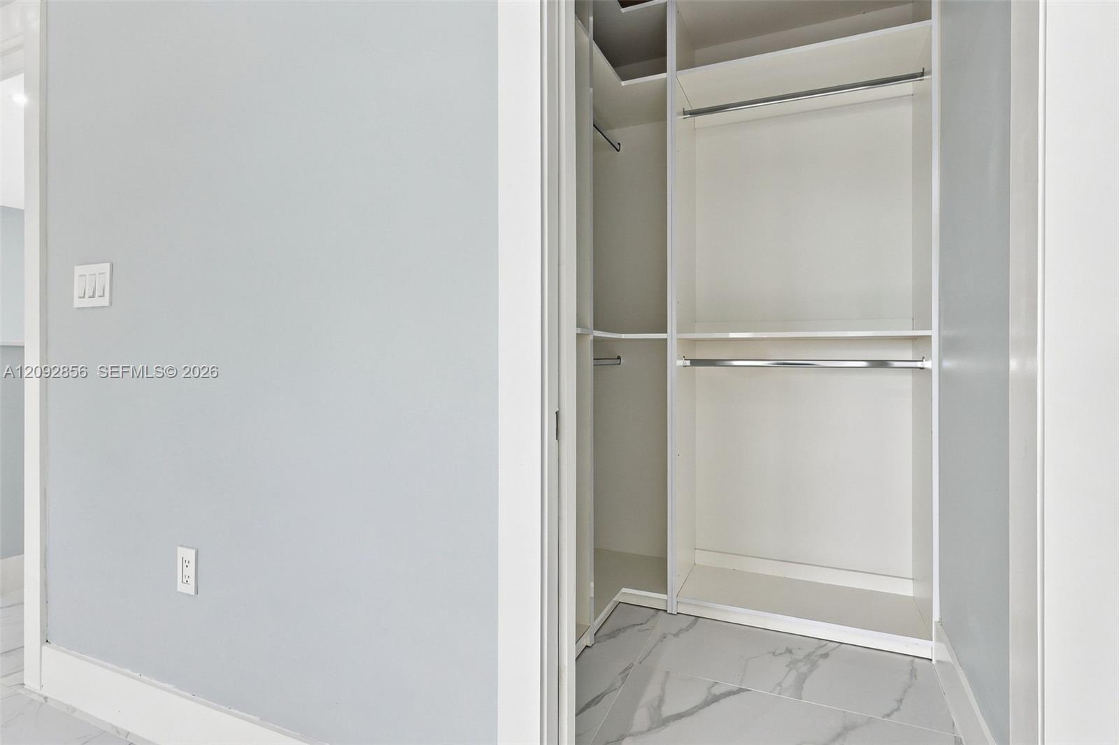 3rd bedroom Walk-in closet featuring white built-in shelving, dual hanging rods, and large-format porcelain tile flooring with marble-finish veining