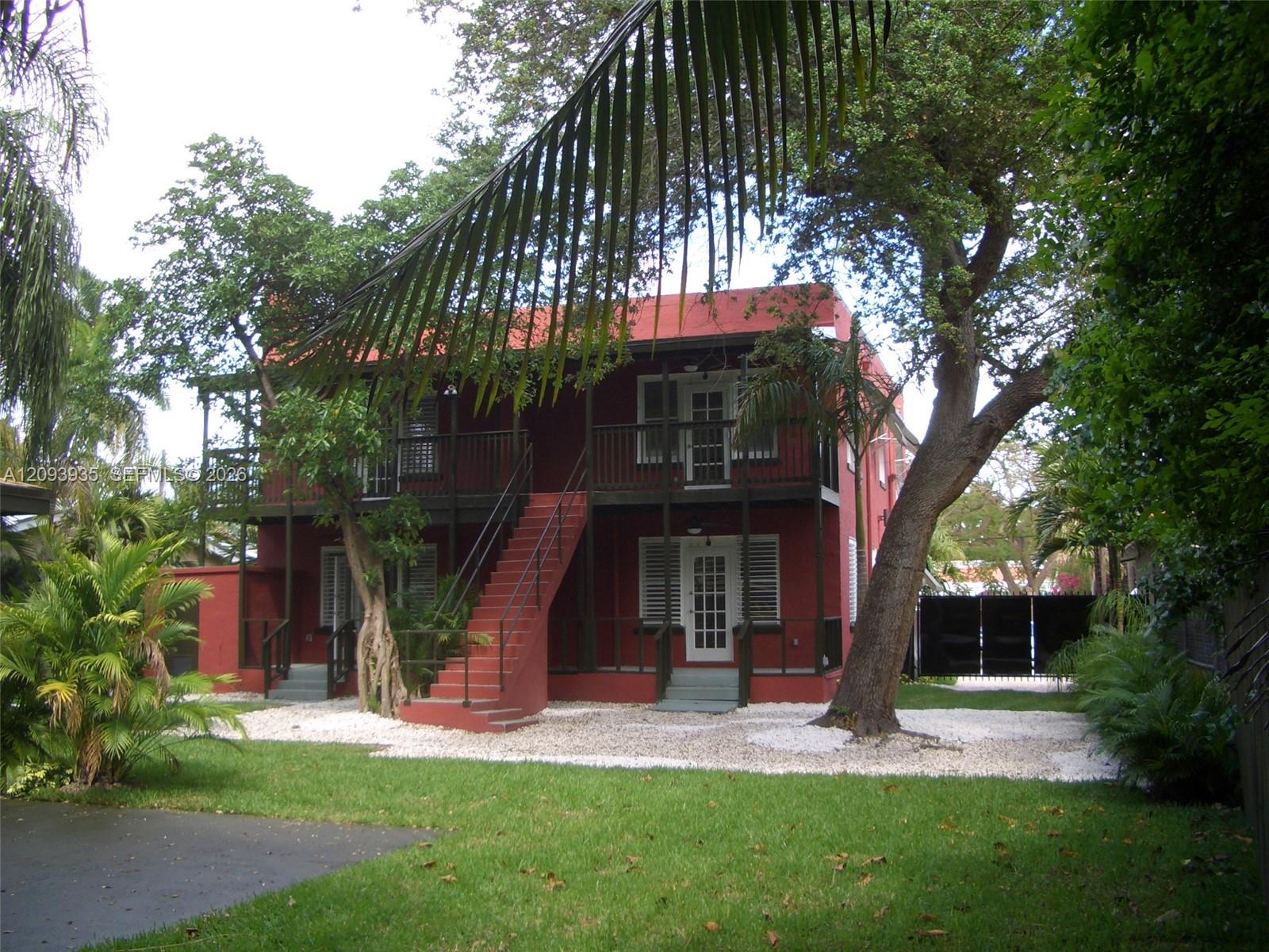 Two-story exterior featuring masonry construction, a multi-level railed balcony, an external staircase, louvered shutters, and mature trees