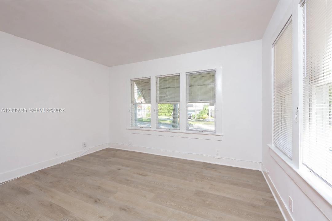 Neutral interior featuring wood-finish flooring, white walls, and multiple windows with horizontal blinds Neutral interior featuring wood-finish flooring, white walls, and multiple windows with horizontal blinds