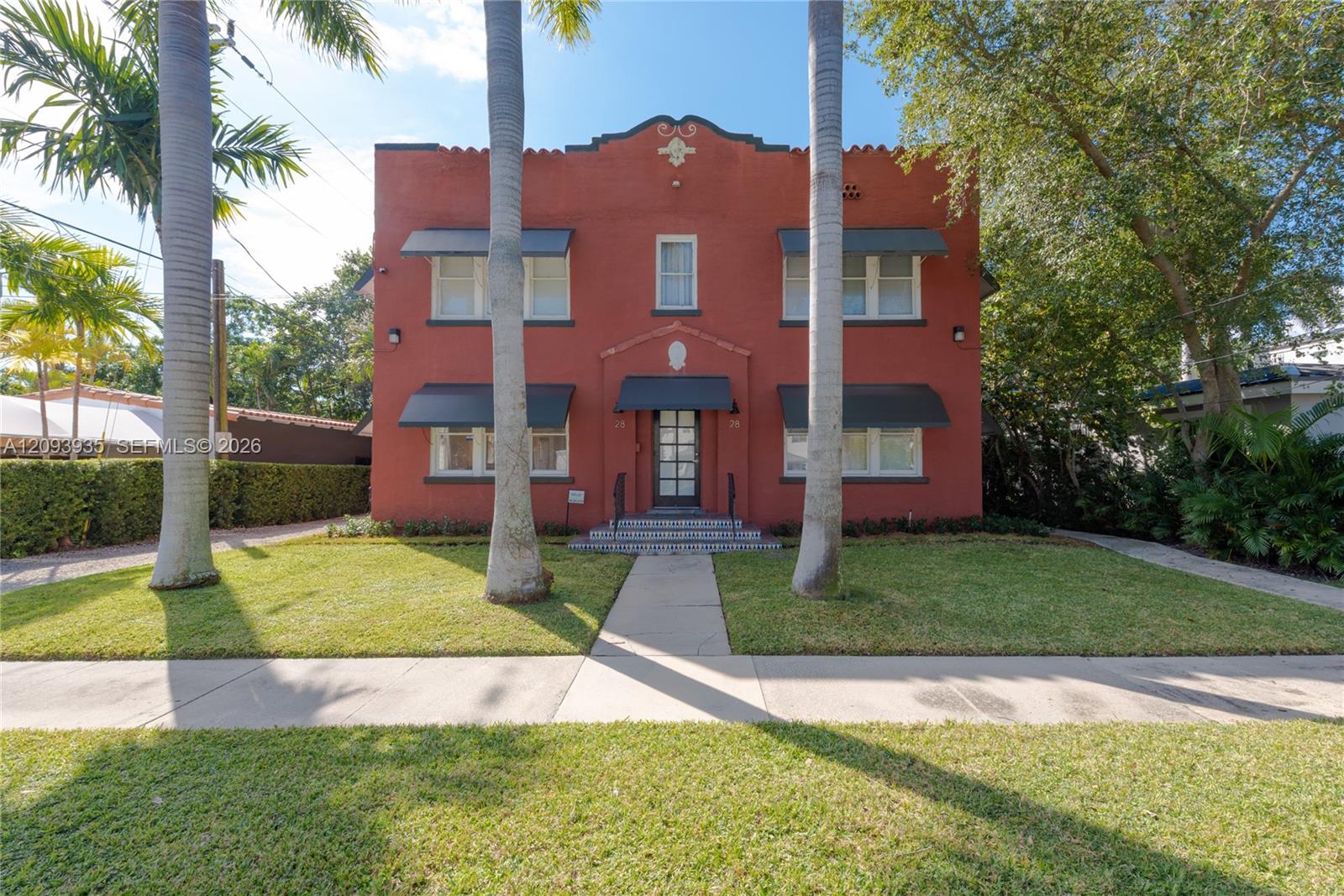 Two-story masonry exterior featuring mission-style architectural details, metal window awnings, symmetrical multi-pane windows, and a covered entry with tiled steps Two-story masonry exterior featuring mission-style architectural details, metal window awnings, symmetrical multi-pane windows, and a covered entry with tiled steps