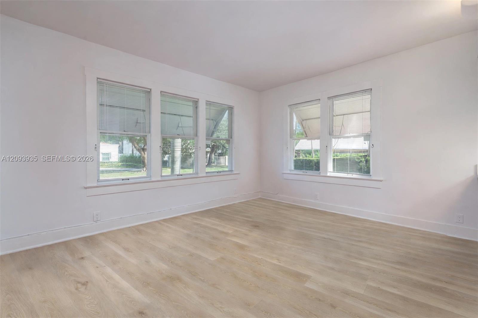 Interior space featuring wood-finish flooring, white walls, and multiple double-hung windows with white casing Interior space featuring wood-finish flooring, white walls, and multiple double-hung windows with white casing