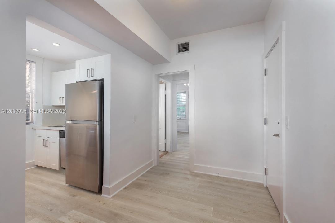 Interior featuring wood-finish flooring, white cabinetry with silver-tone hardware, and a stainless steel refrigerator Interior featuring wood-finish flooring, white cabinetry with silver-tone hardware, and a stainless steel refrigerator