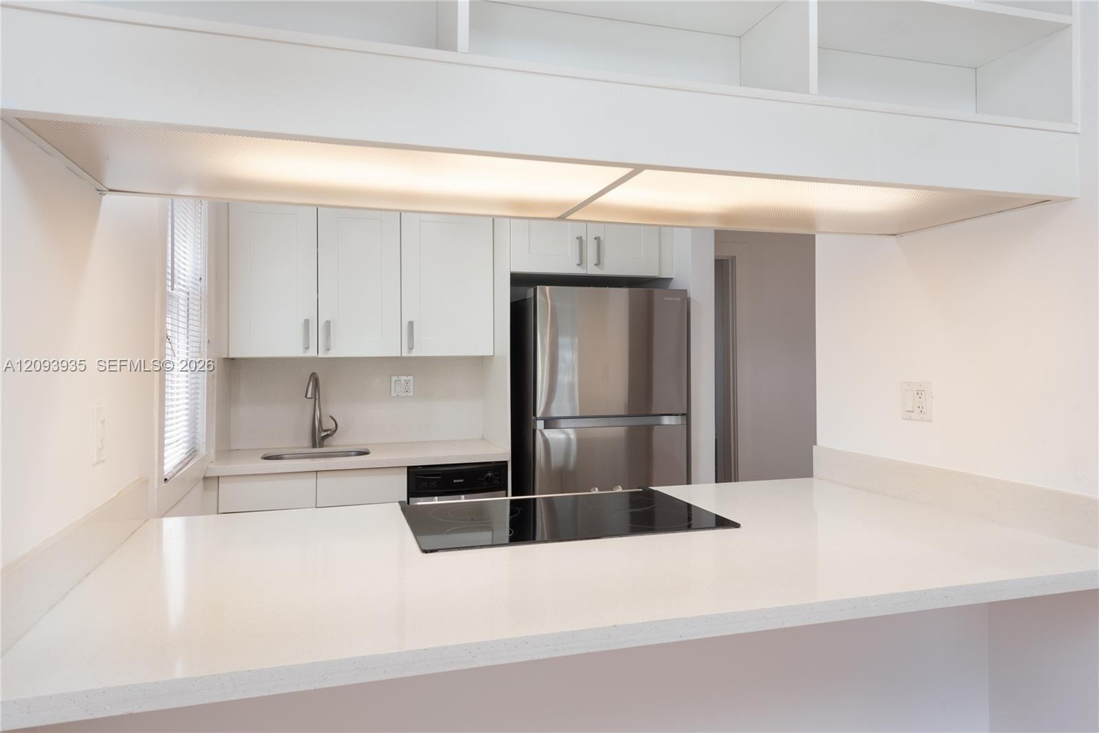 Kitchen featuring white cabinetry, solid-surface countertops, built-in cooktop, stainless steel refrigerator, and integrated under-cabinet lighting