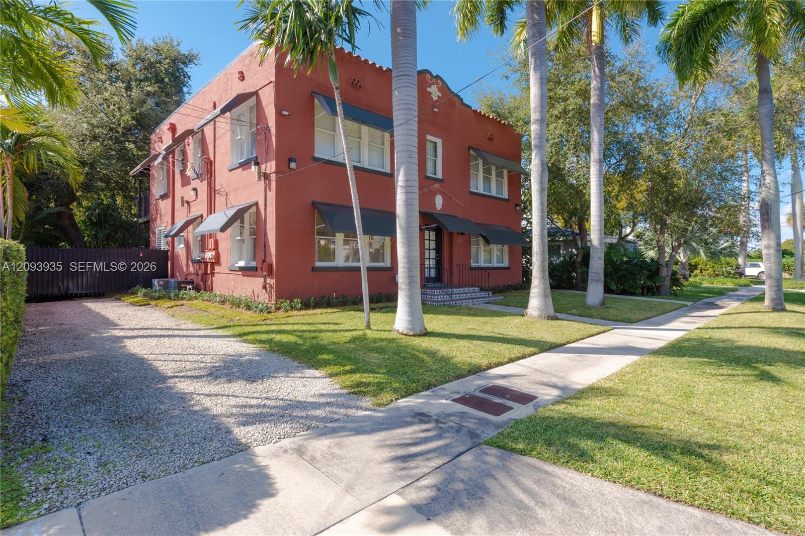 Two-story masonry exterior featuring mission-style architectural details, multiple metal window awnings, and a gravel parking area Two-story masonry exterior featuring mission-style architectural details, multiple metal window awnings, and a gravel parking area