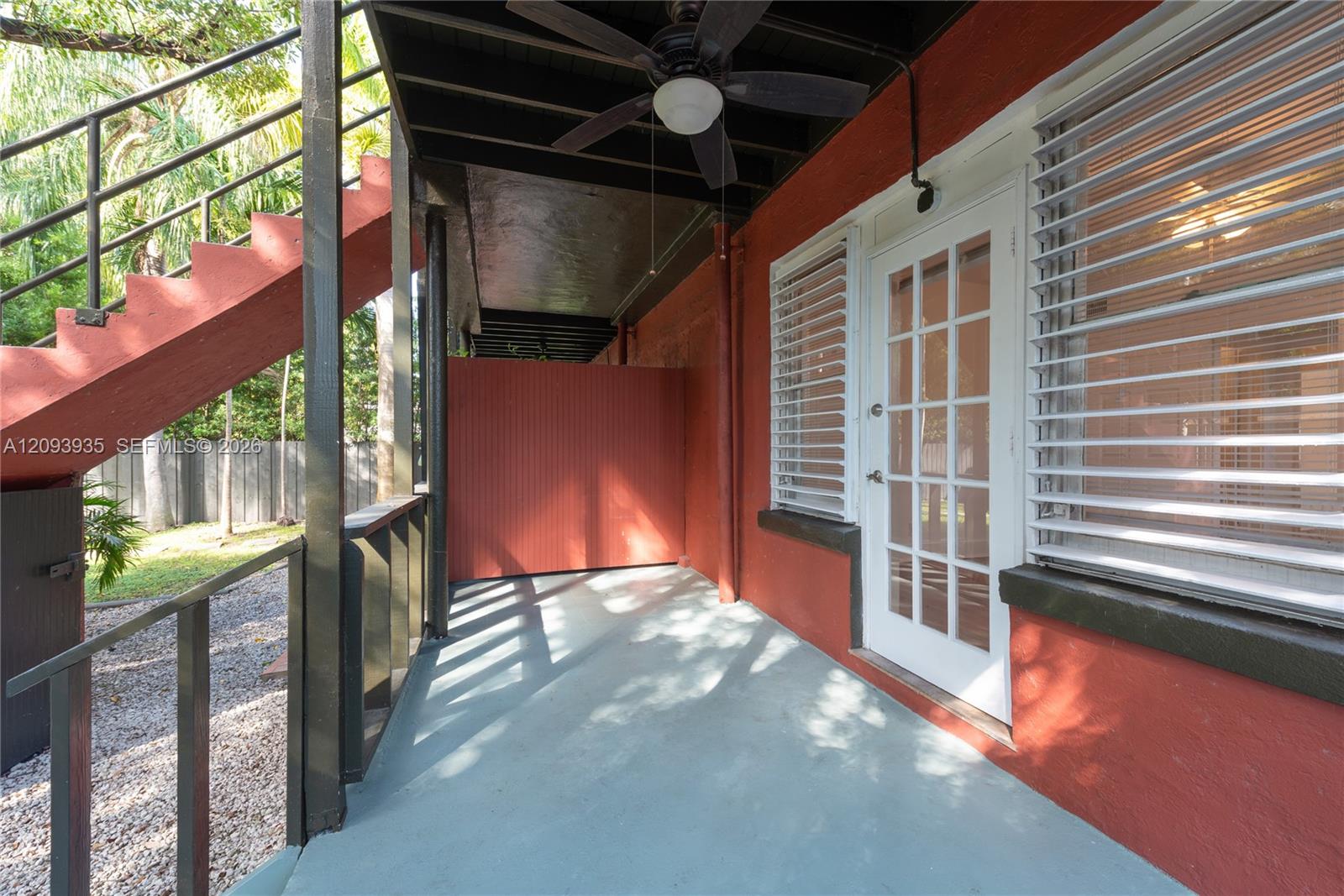 Covered outdoor patio featuring a concrete floor, integrated ceiling fan, glass-panel exterior door, and staircase with metal railings