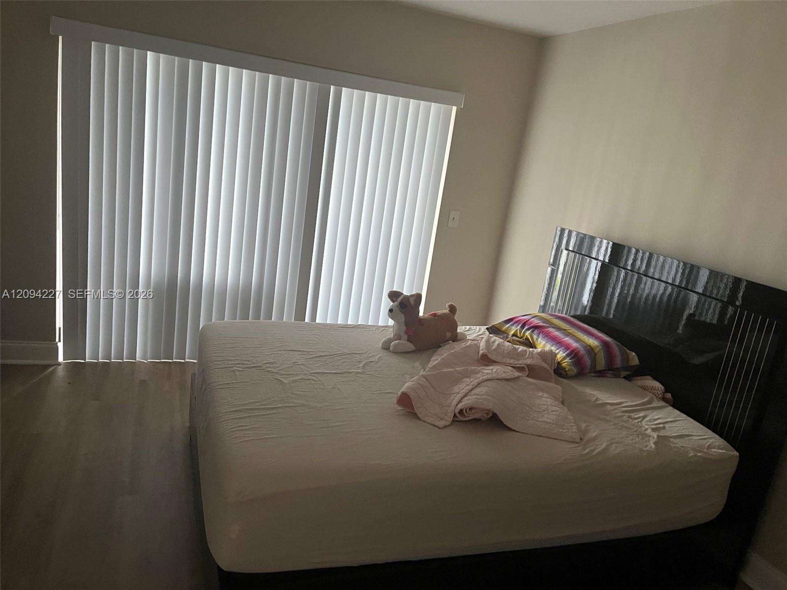 Room featuring wood-finish flooring and large sliding glass doors with vertical blinds