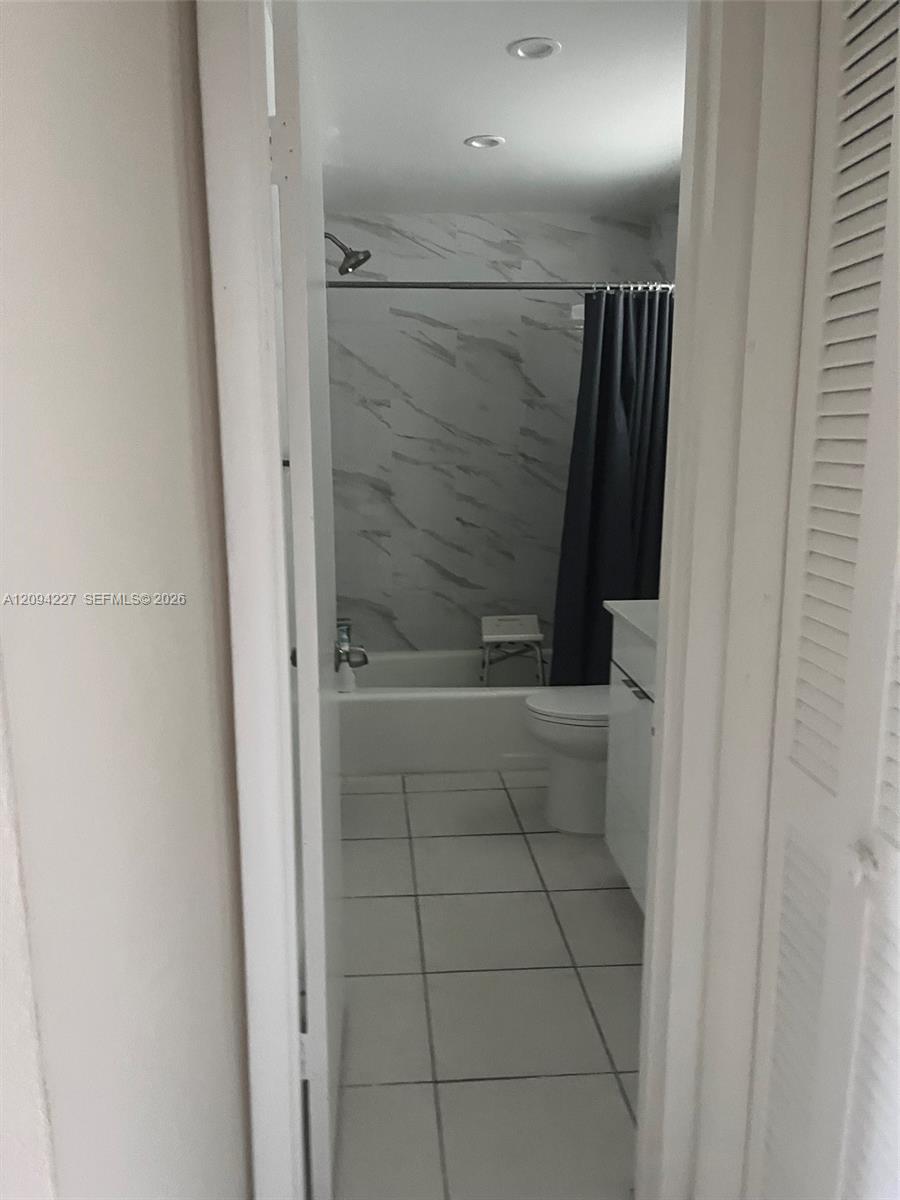 Bathroom featuring large-format floor tiling, a white vanity cabinet, recessed ceiling lighting, and a bathtub surround with full-height decorative wall tile