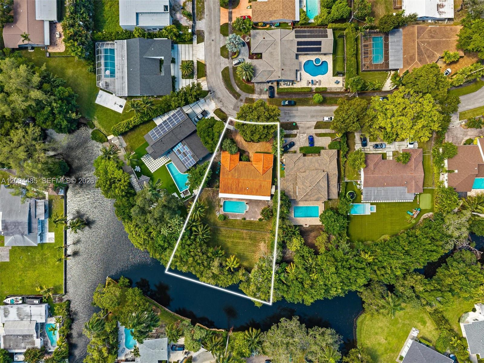 Aerial perspective of a waterfront property featuring a terracotta-tiled roof, a private swimming pool, and an expansive rear lawn area situated along a canal